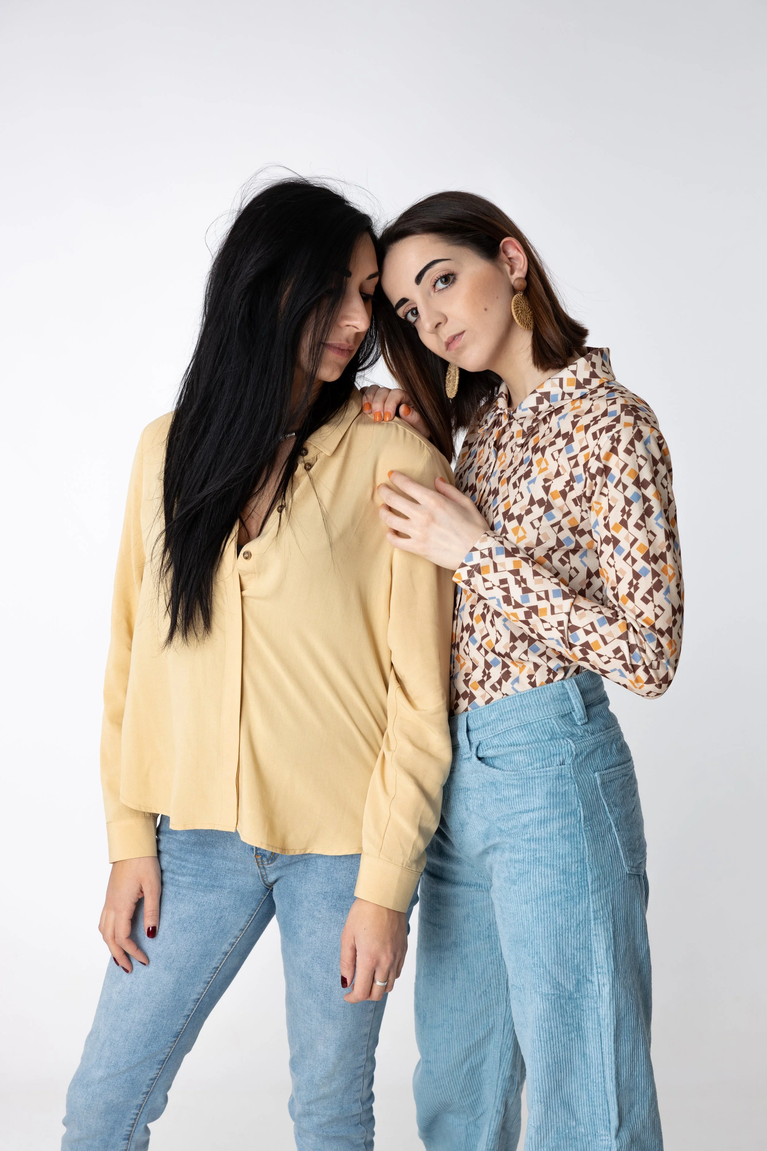 Due donne con abbigliamento casual si abbracciano e guardano verso la fotocamera.