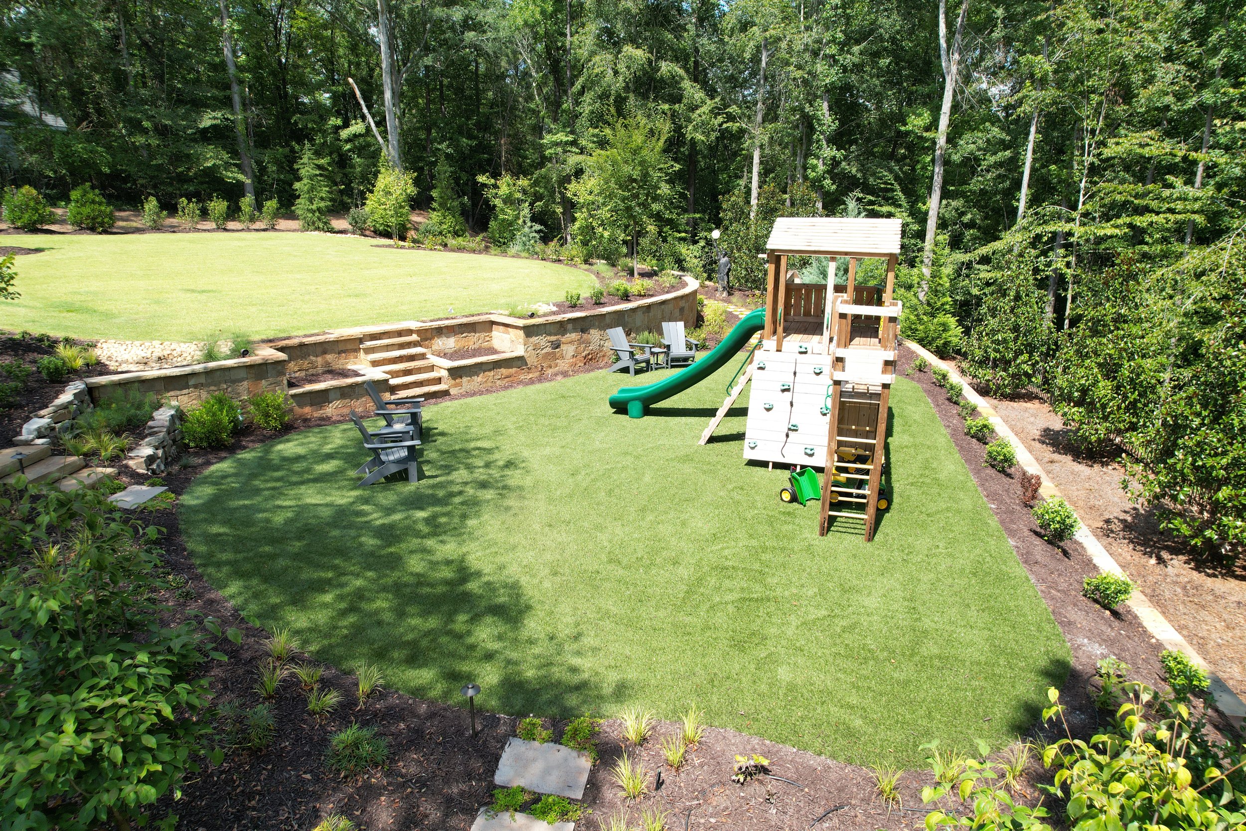 Aerial view of a fully landscaped backyard in Athens Georgia featuring artificial turf, a children's play set, stone retaining walls, terraced sod lawn, and mulch beds by Southern Grounds Landscaping