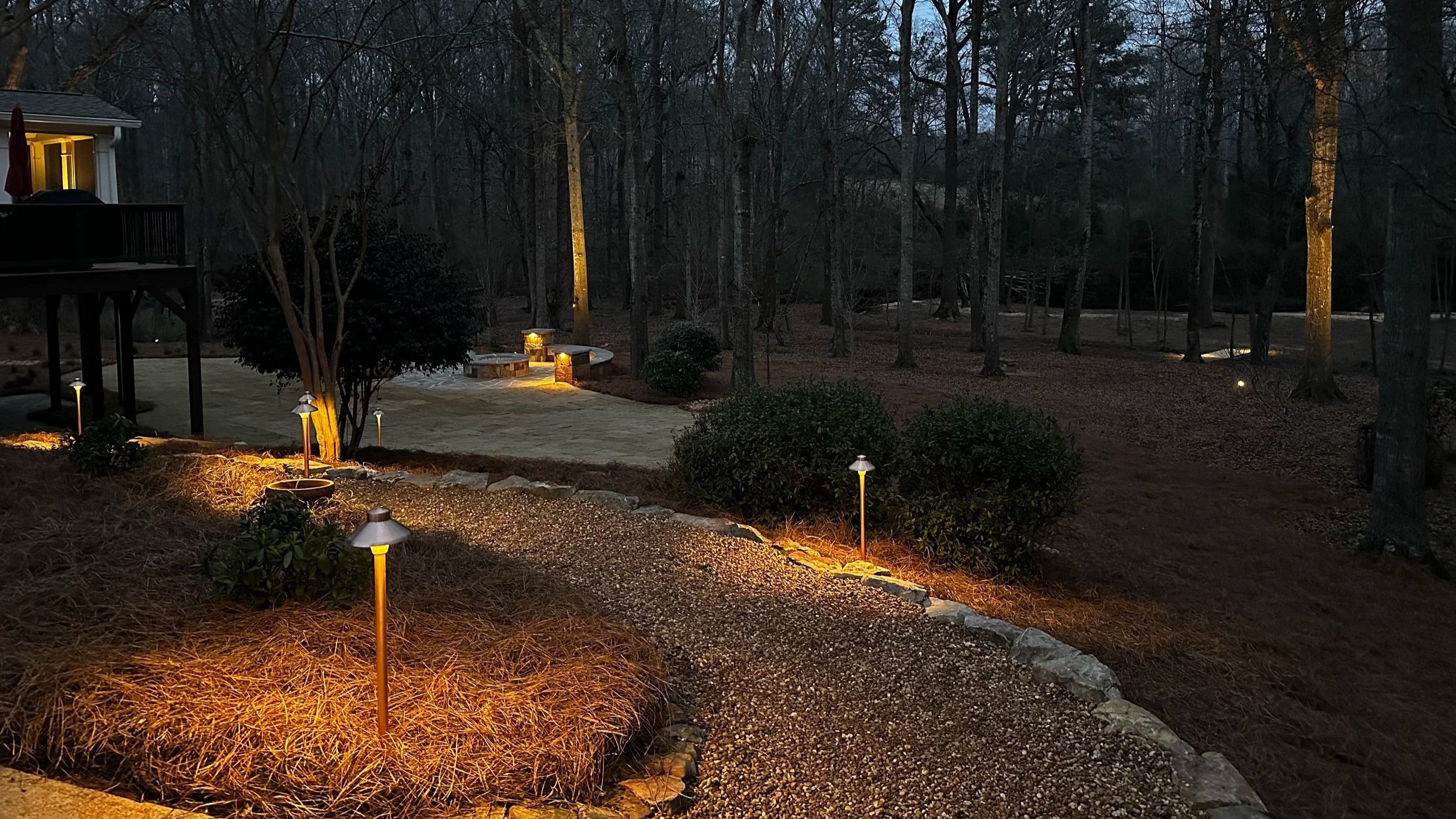 Professionally installed landscape path lighting along pine straw walkway and mulch beds at night by Southern Grounds Landscaping in Watkinsville Georgia