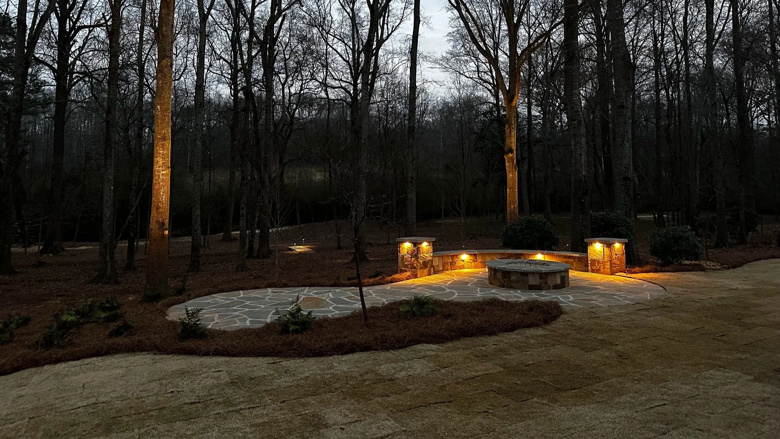 Flagstone fire pit patio with landscape lighting, illuminated for evening entertaining.