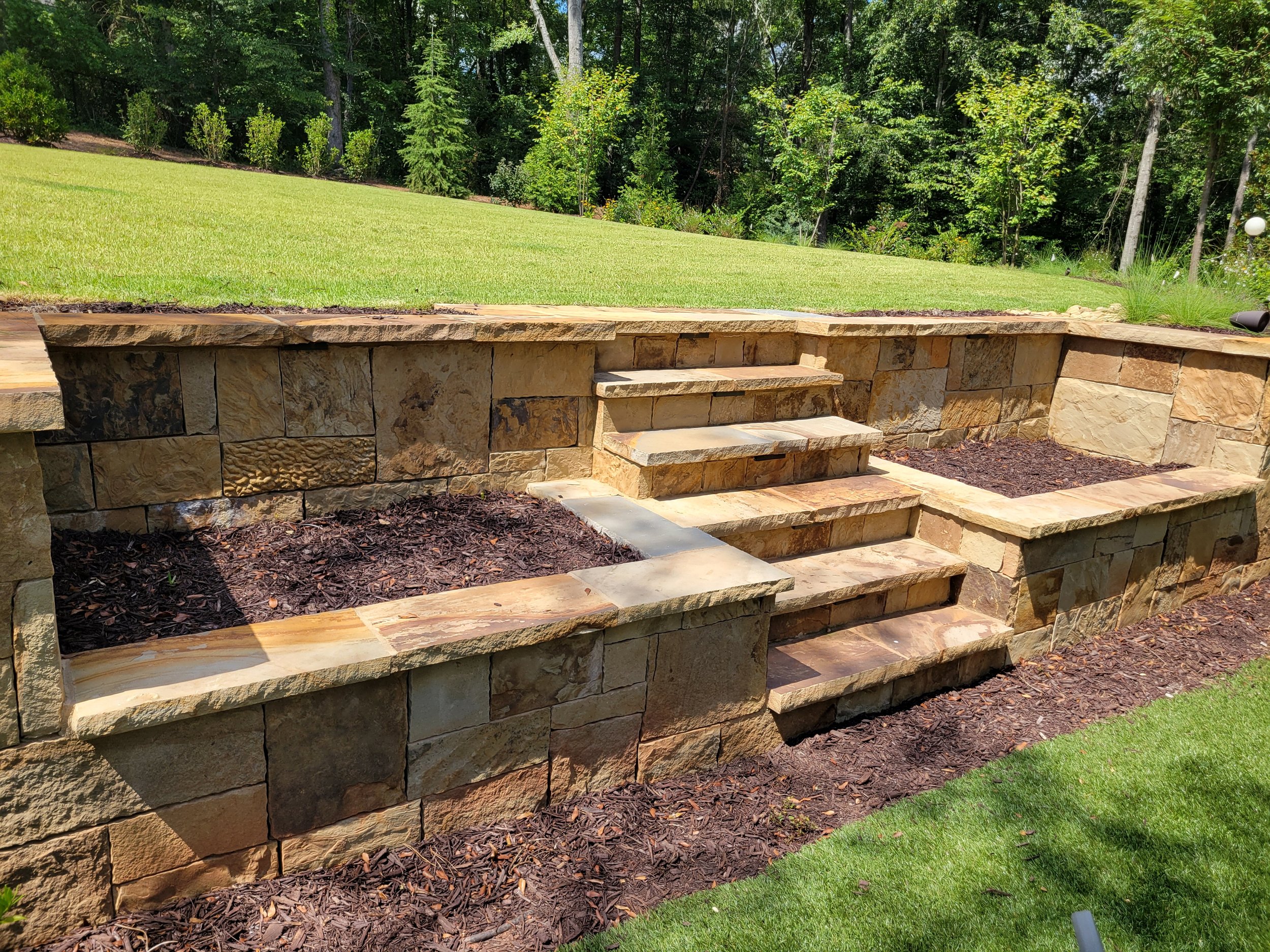 Custom stacked stone retaining wall with built in steps and mulch planting beds installed by Southern Grounds Landscaping in Athens Georgia