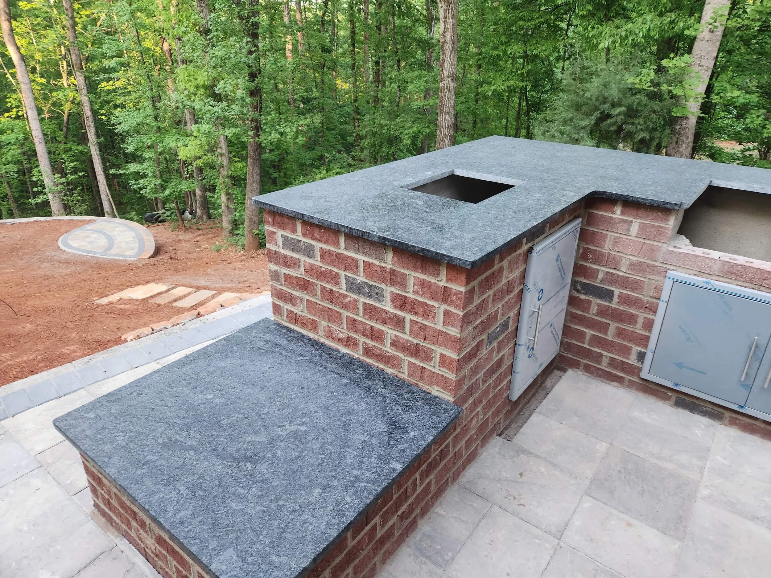 Brick outdoor kitchen island with granite countertops and built-in appliance space on a paver patio.