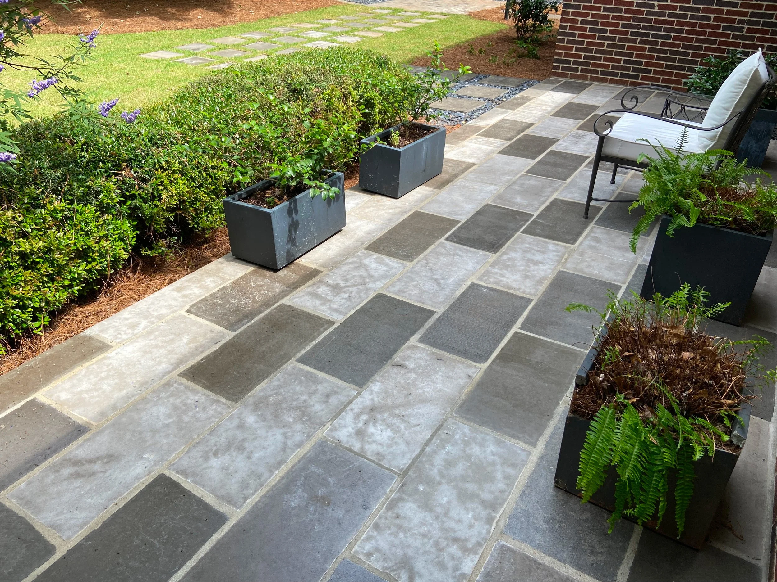 Close up of a custom bluestone and mixed paver patio with decorative planter boxes and ferns installed by Southern Grounds Landscaping in Athens Georgia