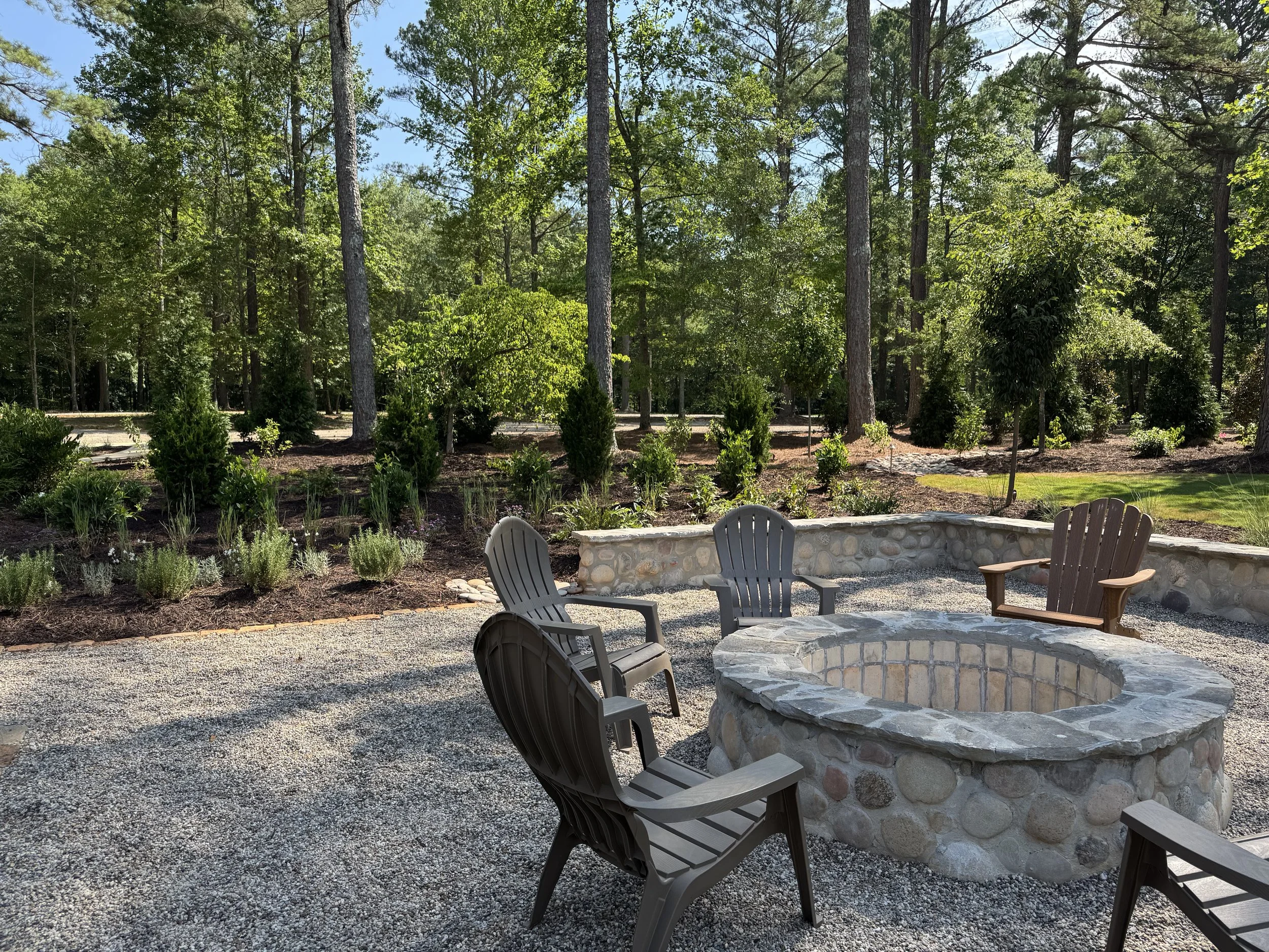 Gravel patio fire pit area with a curved stone retaining wall and fresh landscape plantings.
