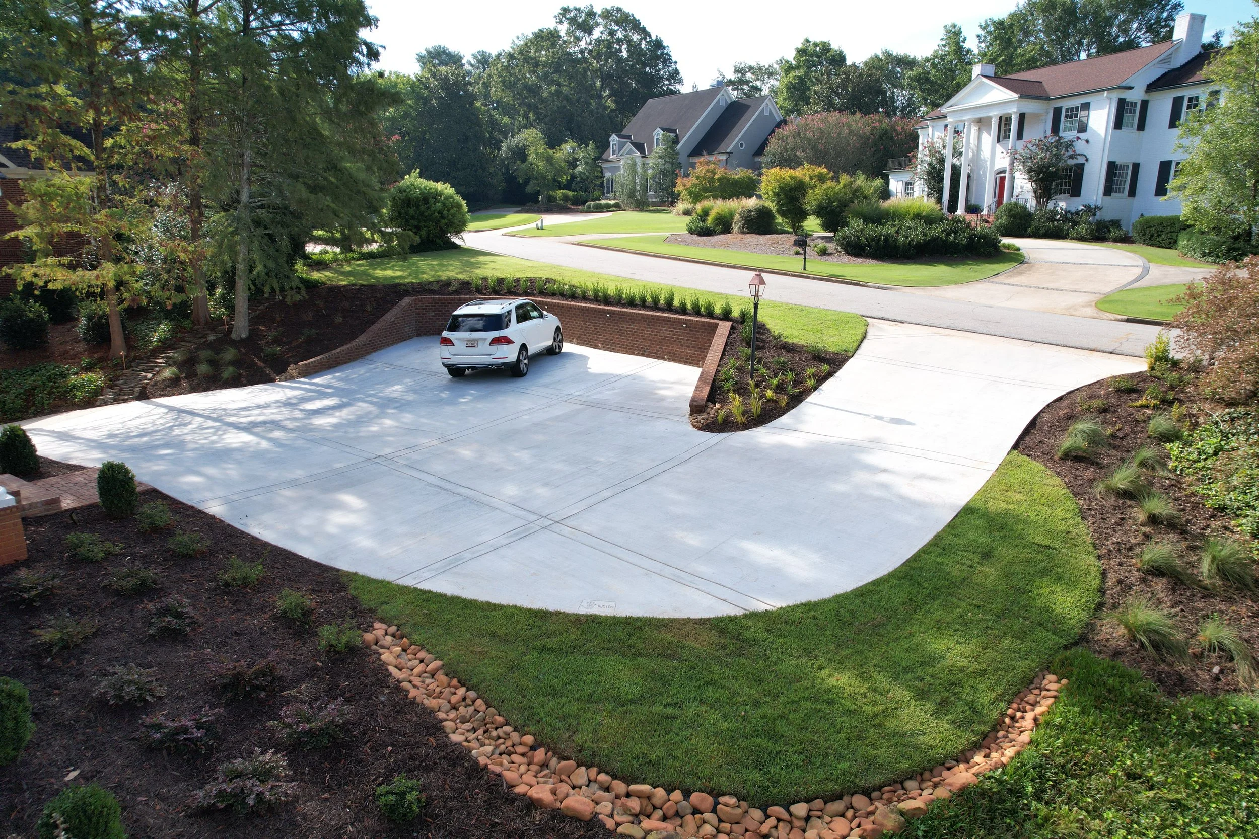 Aerial view of a large concrete turnaround driveway with brick retaining wall, fresh sod, mulch beds, and river rock drainage edging installed by Southern Grounds Landscaping in Athens Georgia