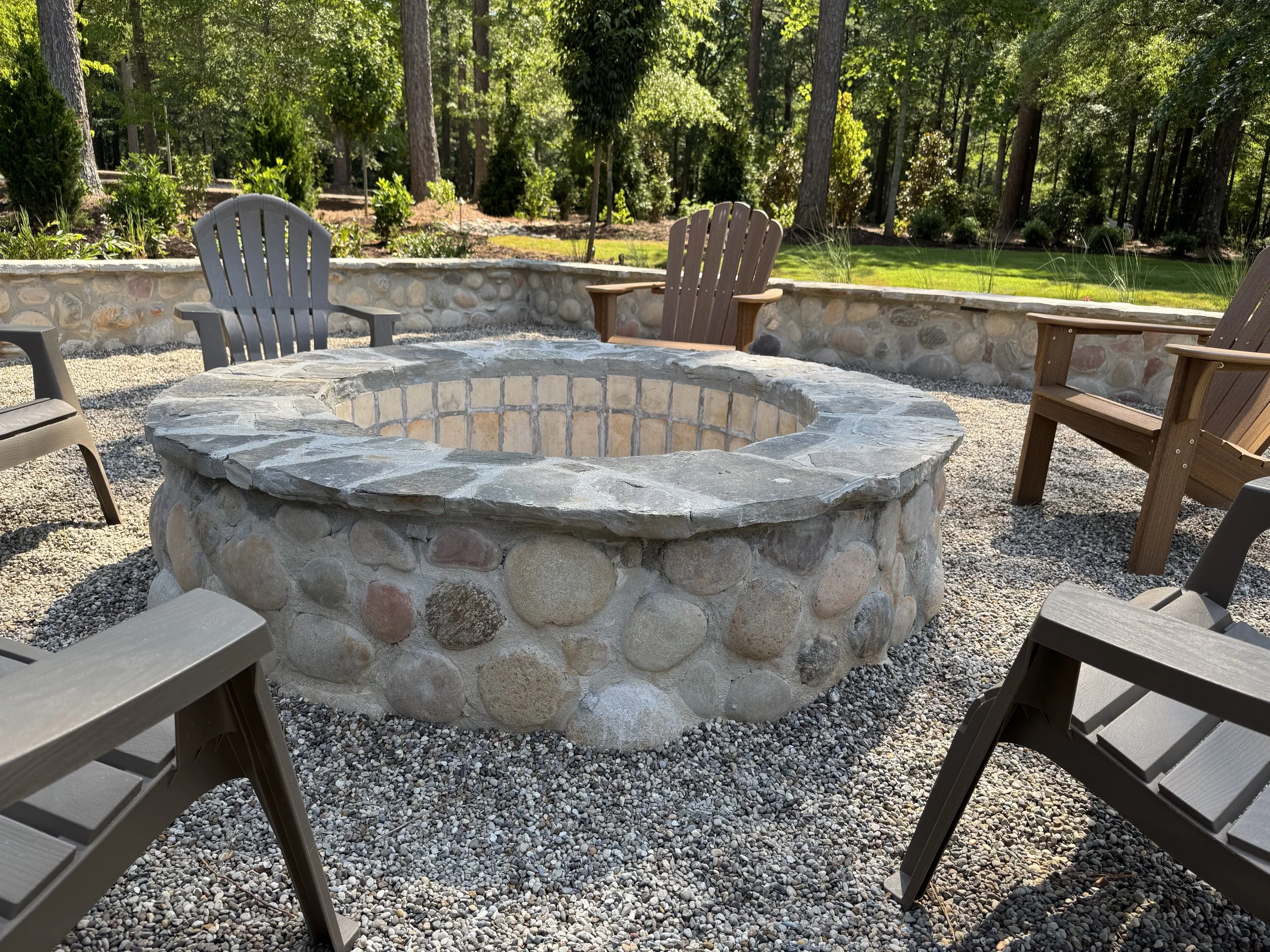 Custom stone and river rock fire pit with Adirondack chairs on a gravel patio installed by Southern Grounds Landscaping in Athens Georgia