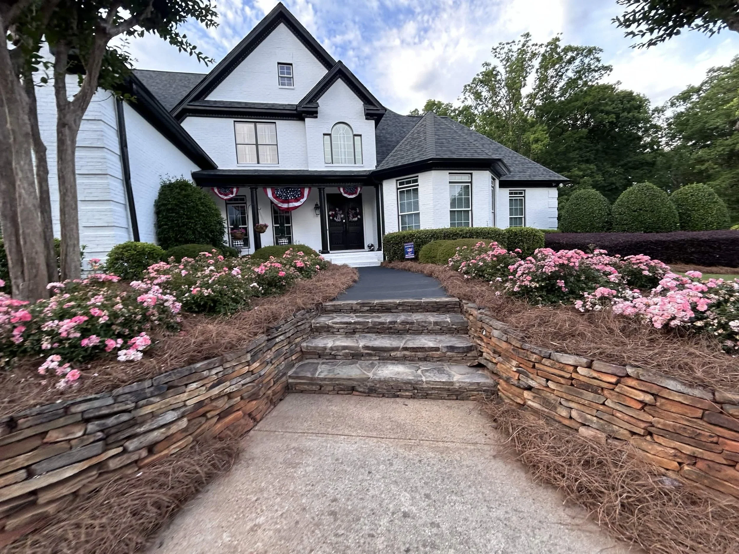 Stacked stone steps flanked by pink rose bushes leading to a home's front entrance.