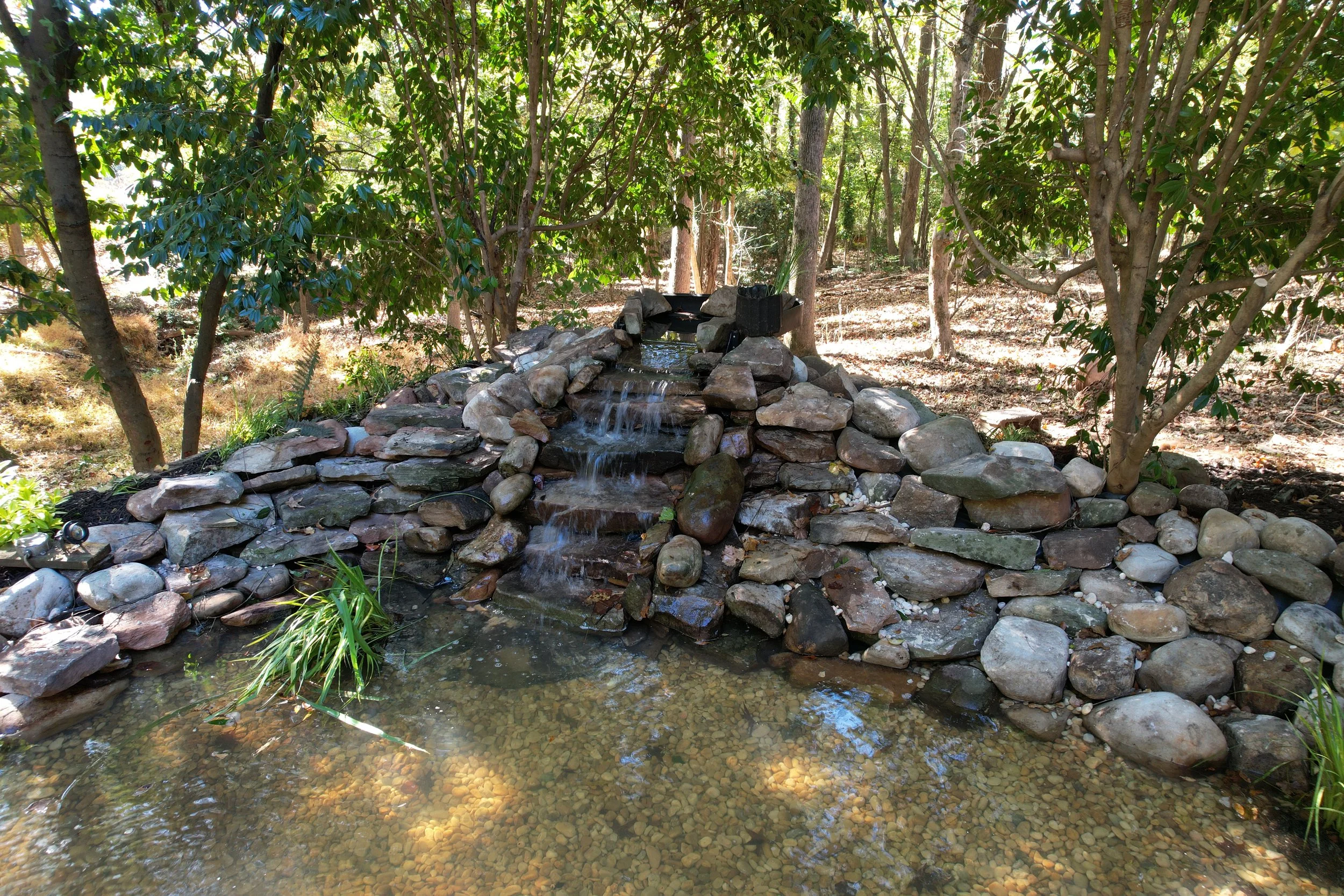 Custom backyard waterfall and pond installation with stacked boulders and river rock by Southern Grounds Landscaping in Athens Georgia