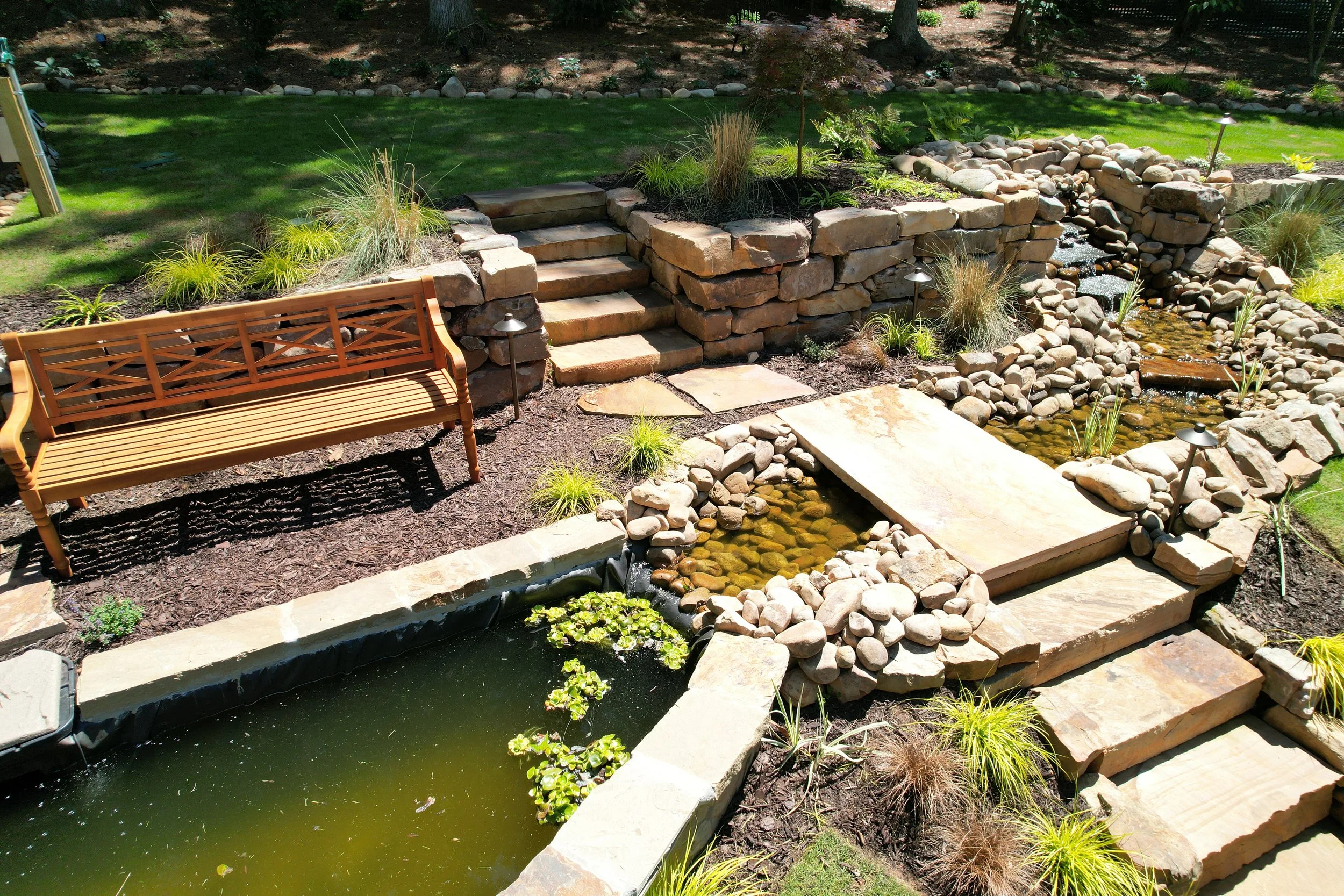 Aerial view of a tiered koi pond with stone waterfall, stepping stones, and stacked stone steps.