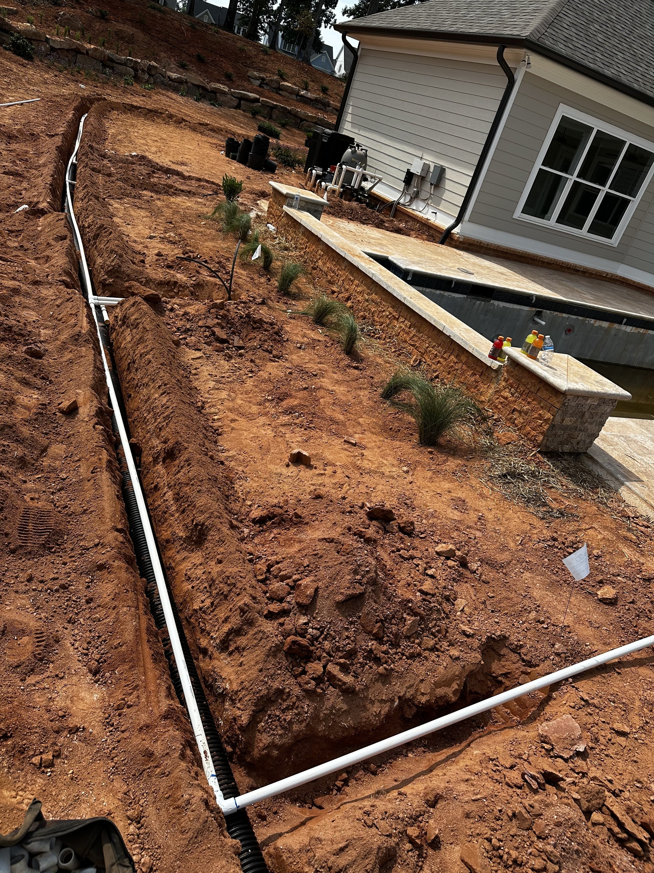 Irrigation trench and pipe installation in progress along a retaining wall near a residential pool by Southern Grounds Landscaping in Lake Oconee Georgia