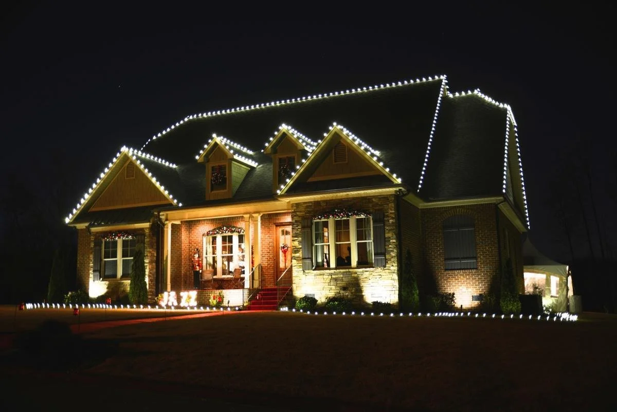 Custom holiday roofline lighting and up-light installation outlining home peaks and gutters