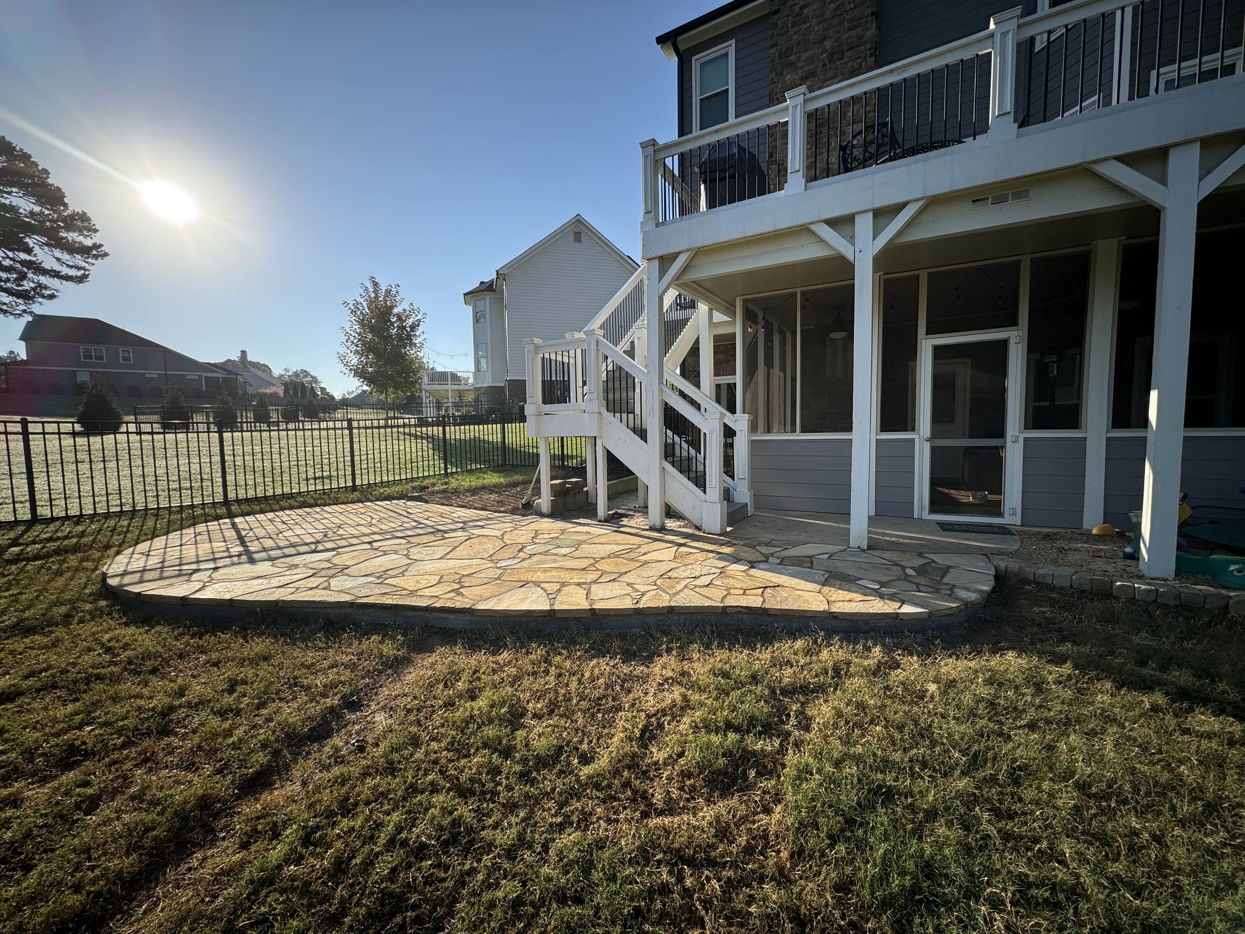 Round flagstone patio bordered in stone beneath an elevated deck and screened porch.