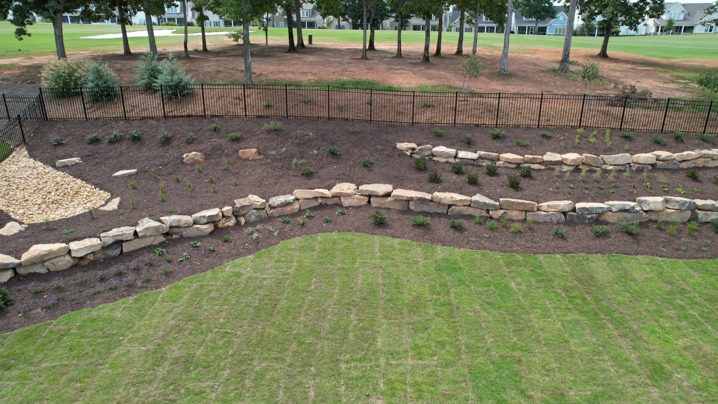 Aerial view of a natural stone retaining wall with fresh mulch beds and newly planted shrubs on a golf course property in Greensboro Georgia by Southern Grounds Landscaping