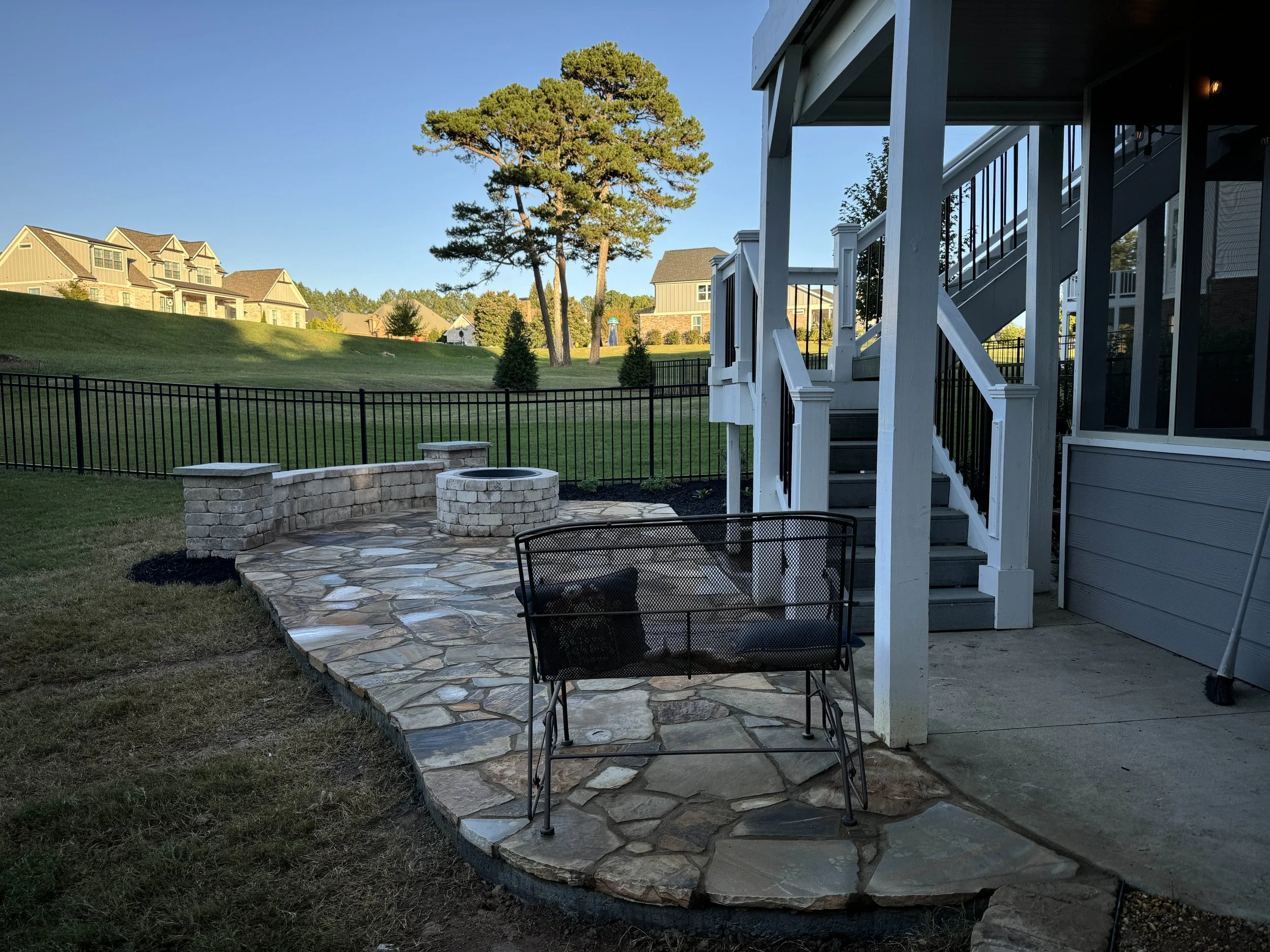 Flagstone patio with stone seat wall and outdoor seating beside a covered porch and staircase.