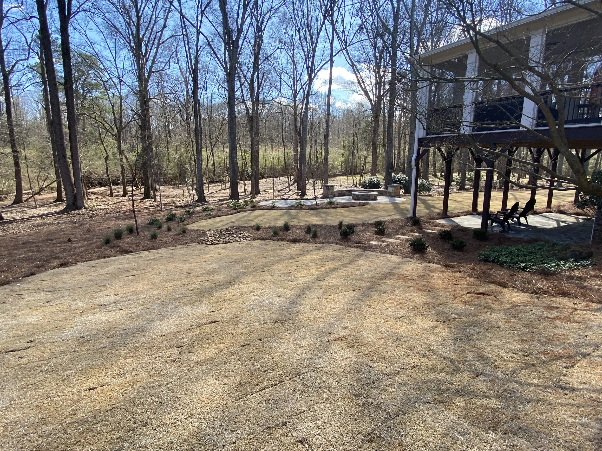 Newly landscaped backyard with hydroseeded lawn, mulch beds, stone fire pit area, and flagstone patio installed by Southern Grounds Landscaping in Watkinsville Georgia