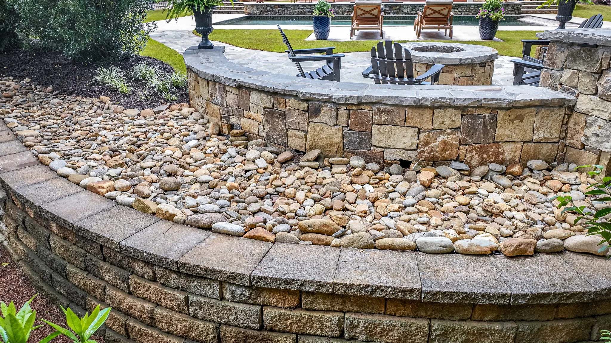 River rock accent wall beneath a stacked stone seat wall bordering a pool patio.