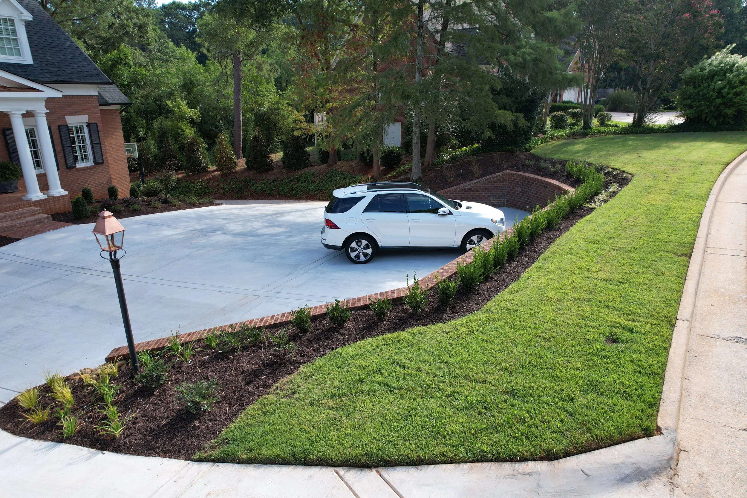Concrete turnaround driveway with brick retaining wall, mulch beds, and newly planted shrubs installed by Southern Grounds Landscaping in Athens Georgia
