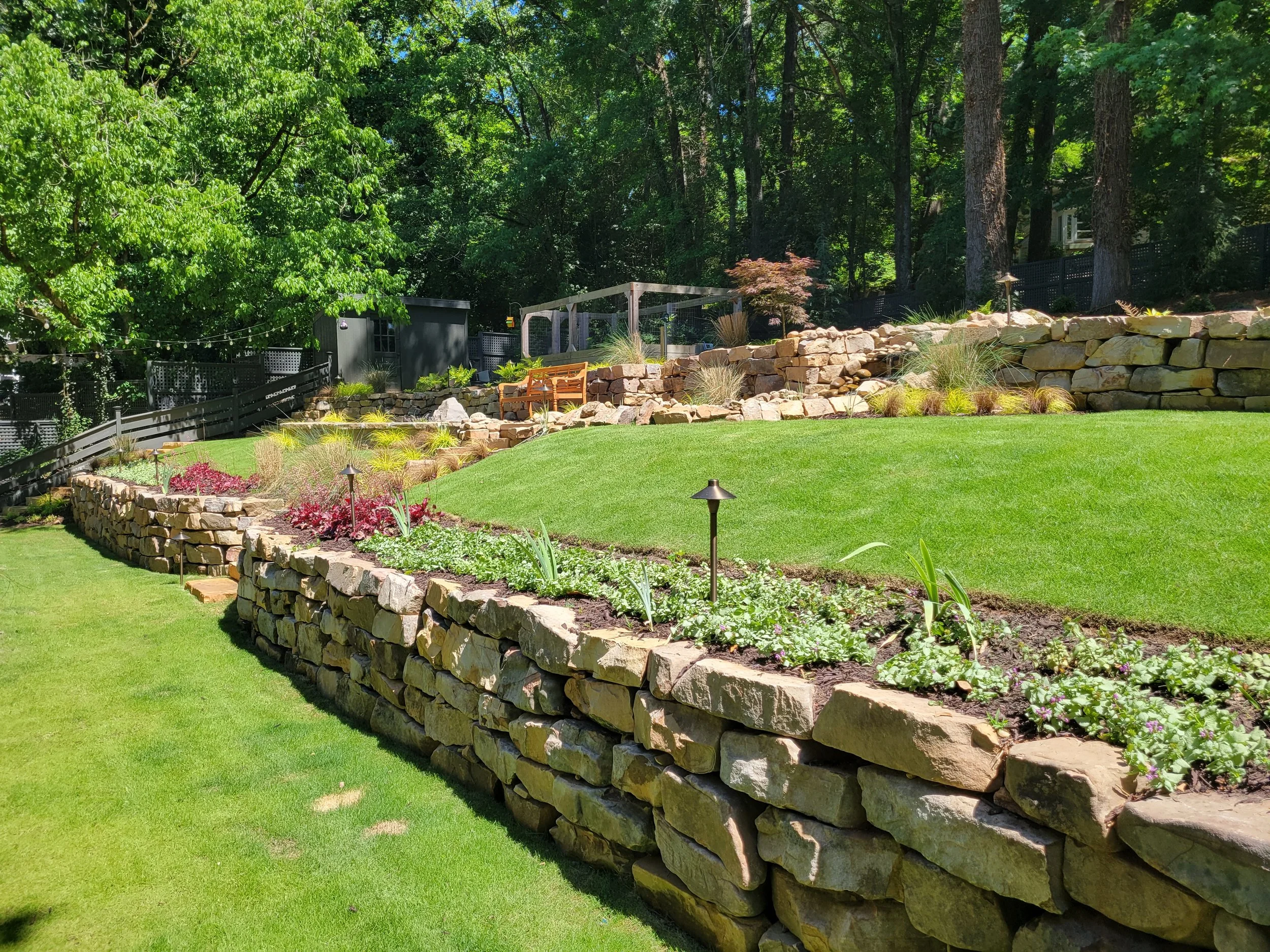 Curved natural stone retaining wall with flower bed landscaping along manicured lawn