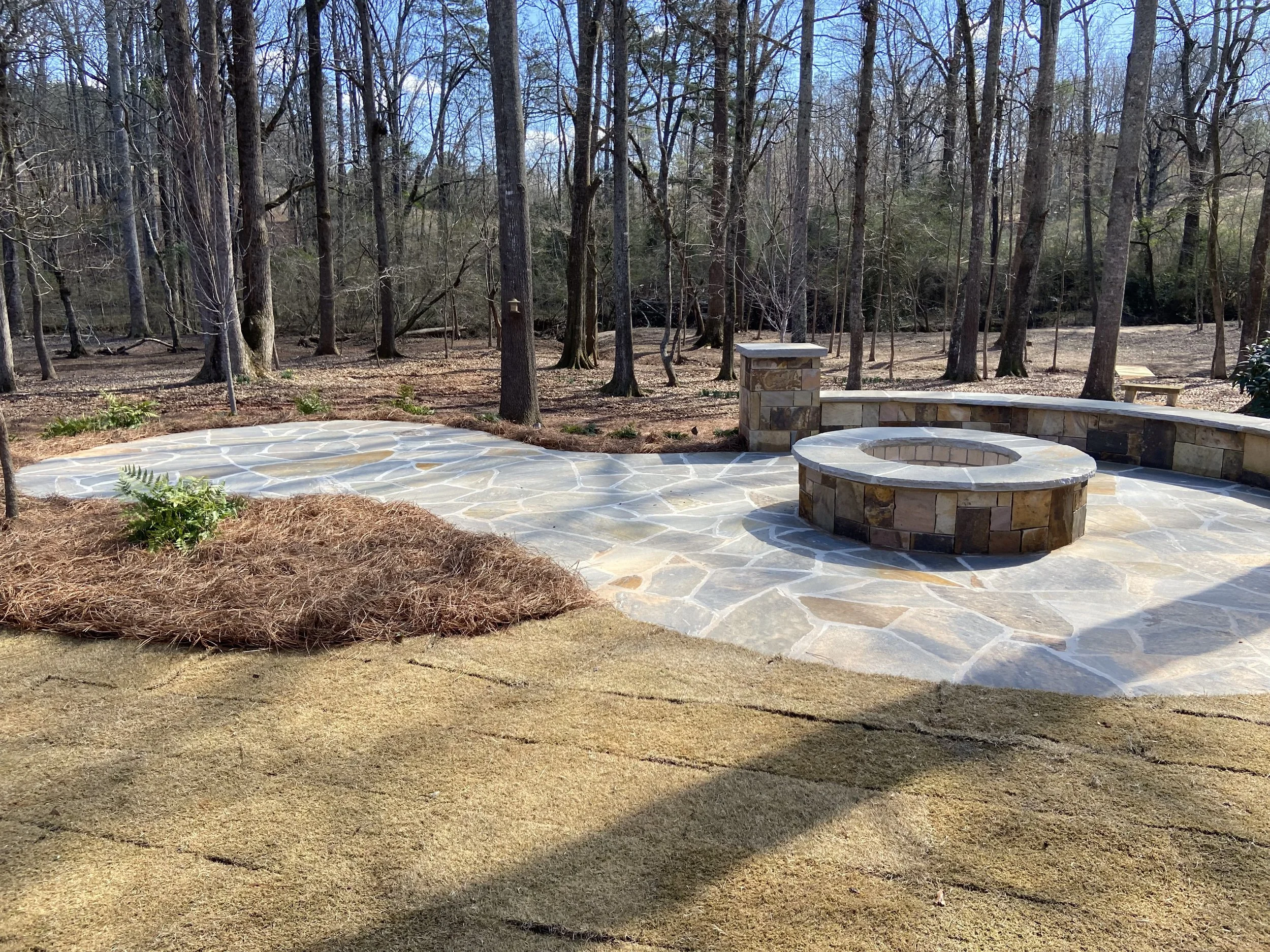 Custom flagstone patio with stone fire pit and curved seating wall installed by Southern Grounds Landscaping in Watkinsville Georgia