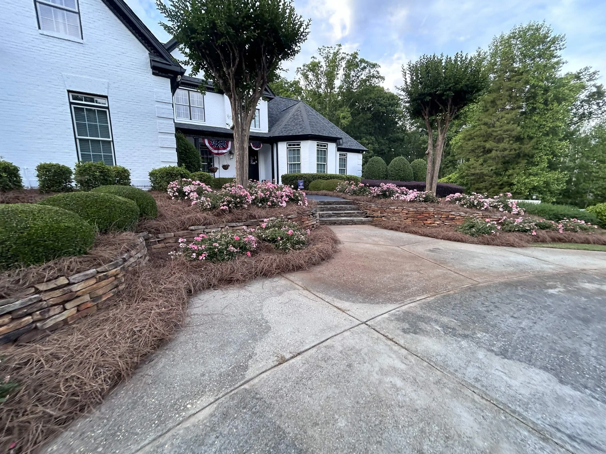Curved stone retaining wall with blooming rose bushes lining a circular driveway entrance.