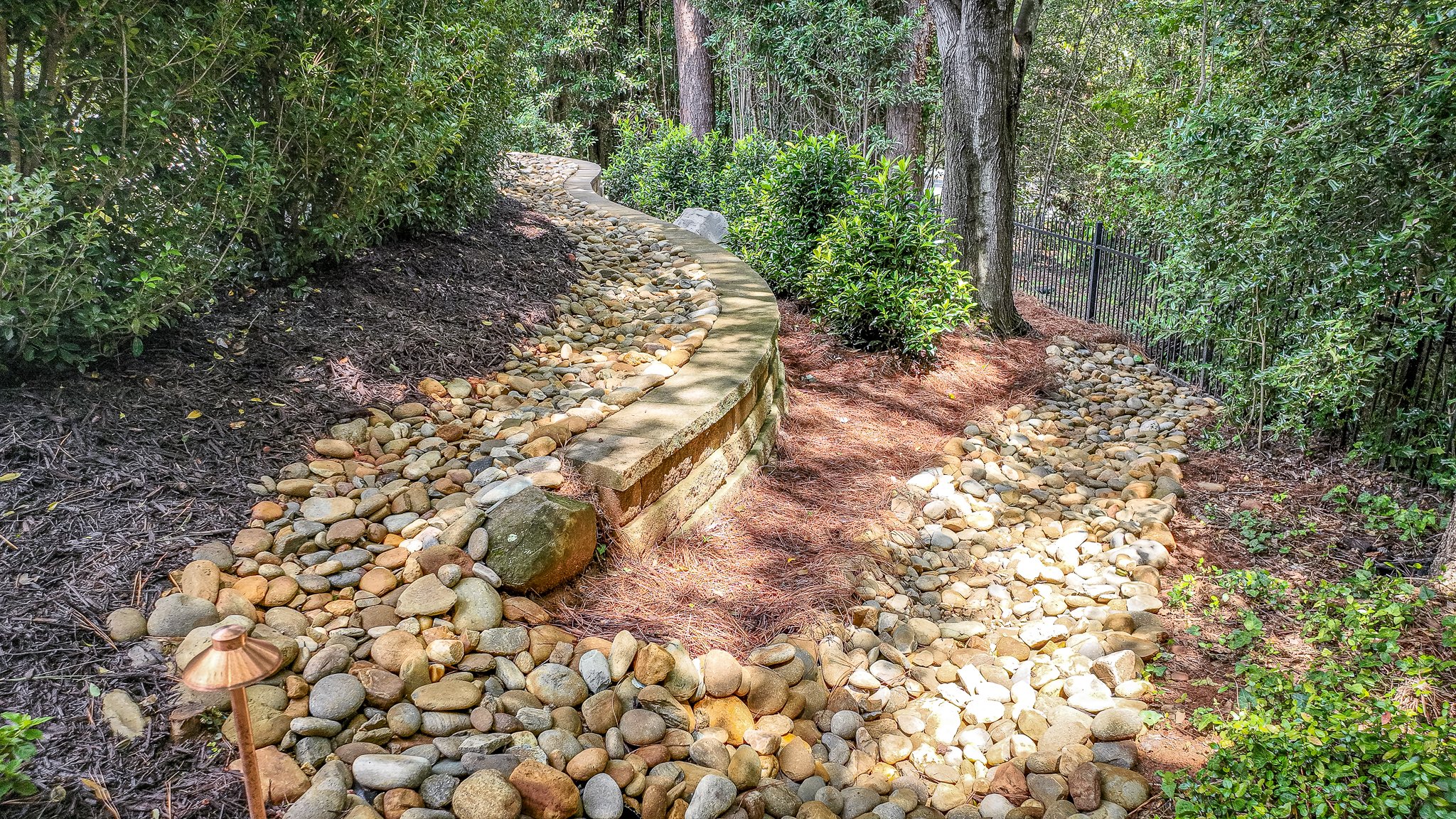 River rock dry creek bed paired with a natural stacked stone retaining wall along a mulched garden path.