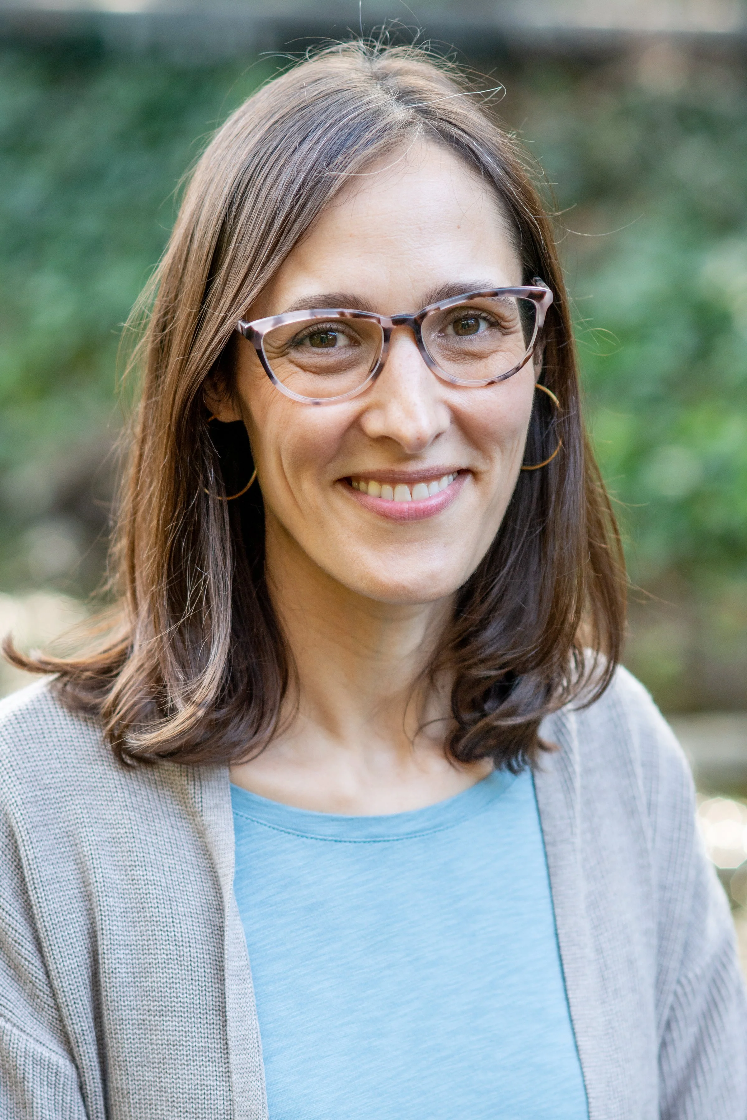 Lara Clayman outdoors, wearing sweater and glasses, warm smile