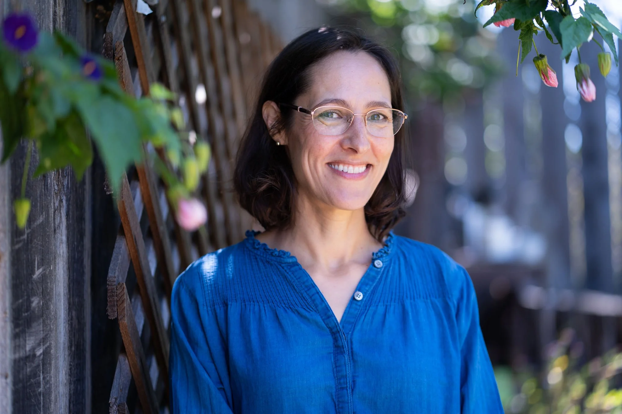 Lara Clayman head slightly turned, glasses, brown hair, with friendly smile, standing in garden