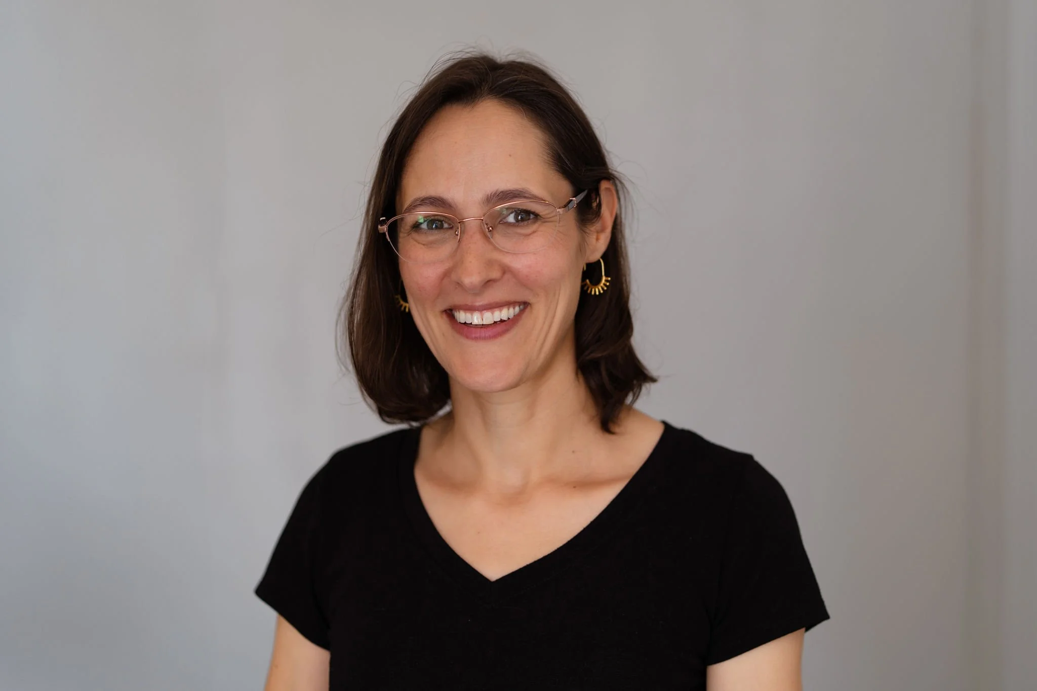 Lara Clayma, smiling, black t-shirt, glasses in front of neutral background