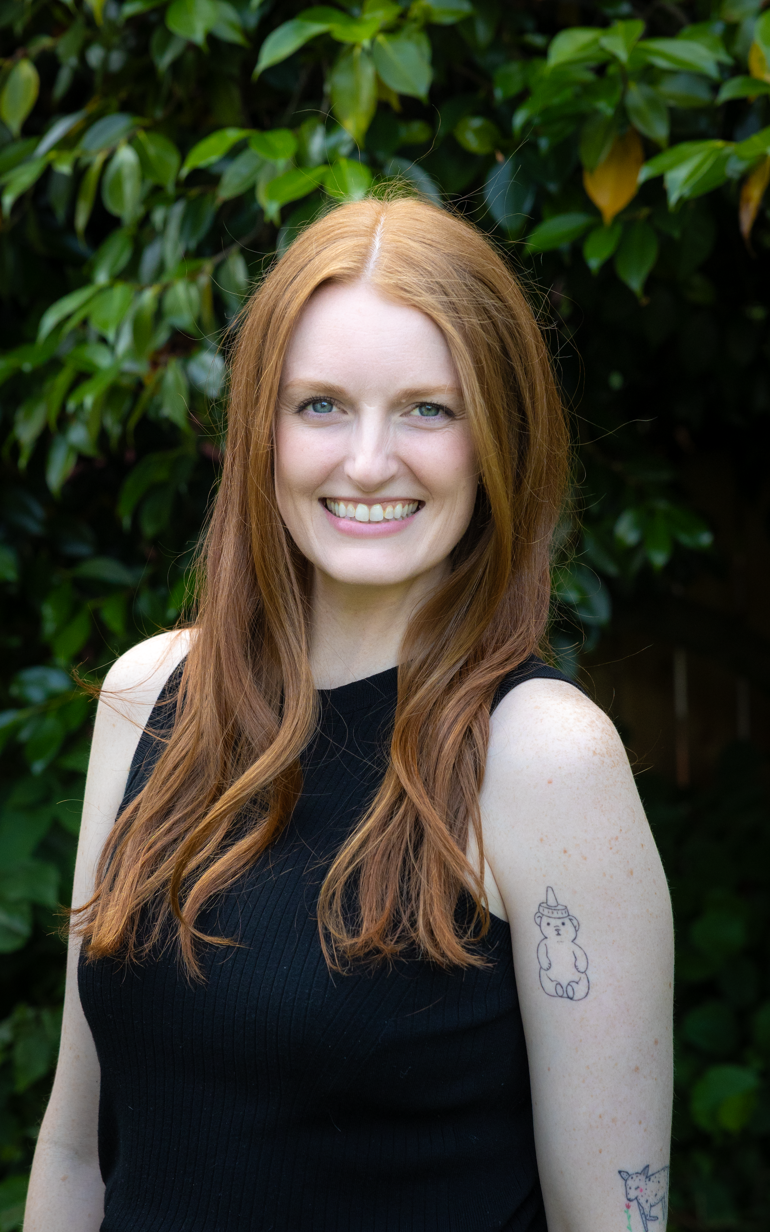 A woman with long red hair and a white shirt smiling while holding a golden retriever puppy with floppy ears and a red collar outdoors near a blue mural.