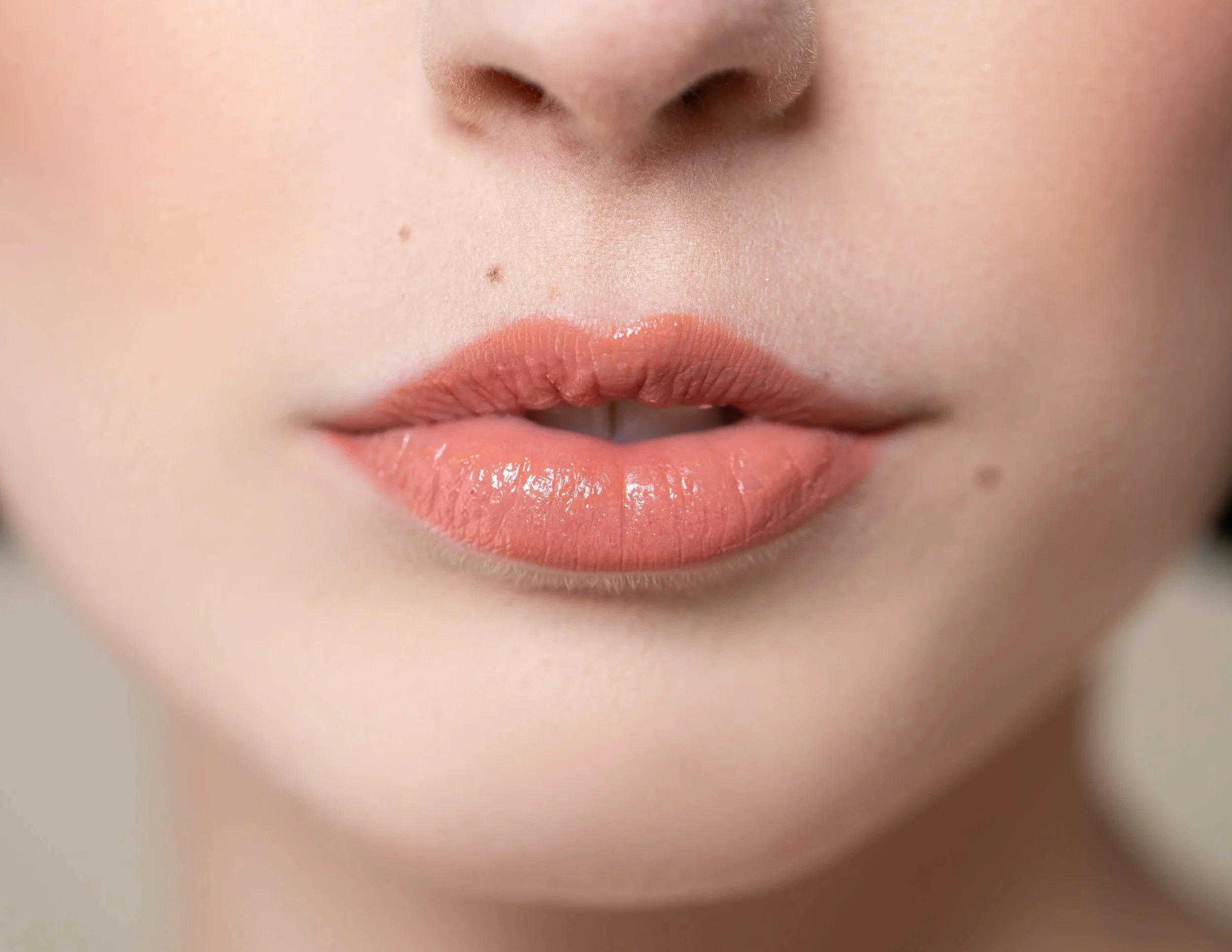 Close-up of a person's lips with glossy peach lipstick and clear skin.