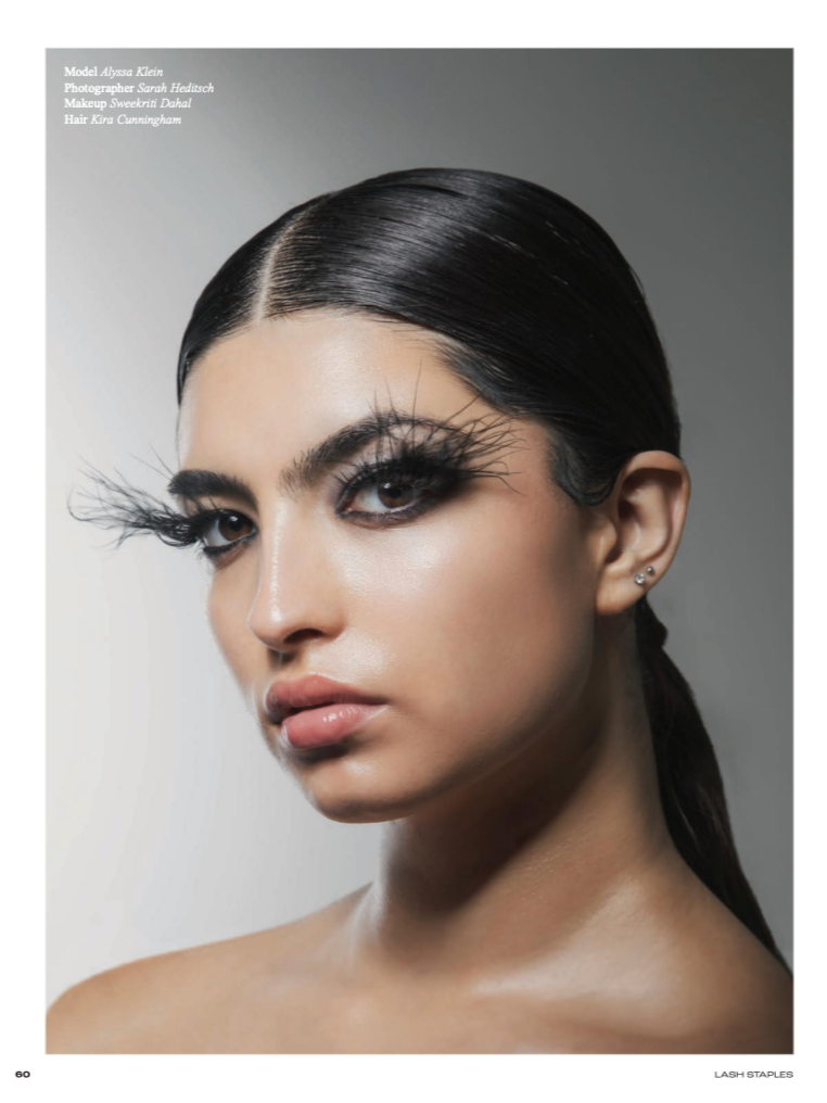 Close-up portrait of a woman with sleek, straight dark hair, dramatic false eyelashes, and natural makeup, against a plain background.