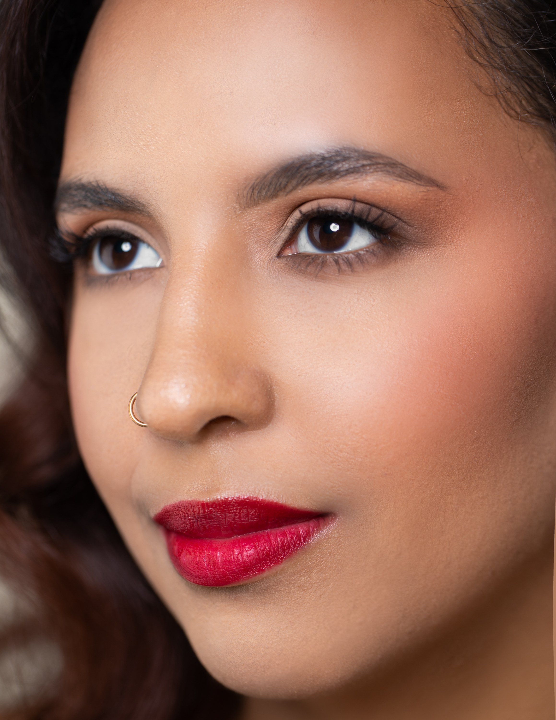 Close-up of a woman's face with makeup, including red lipstick, eye makeup, and a small nose ring.