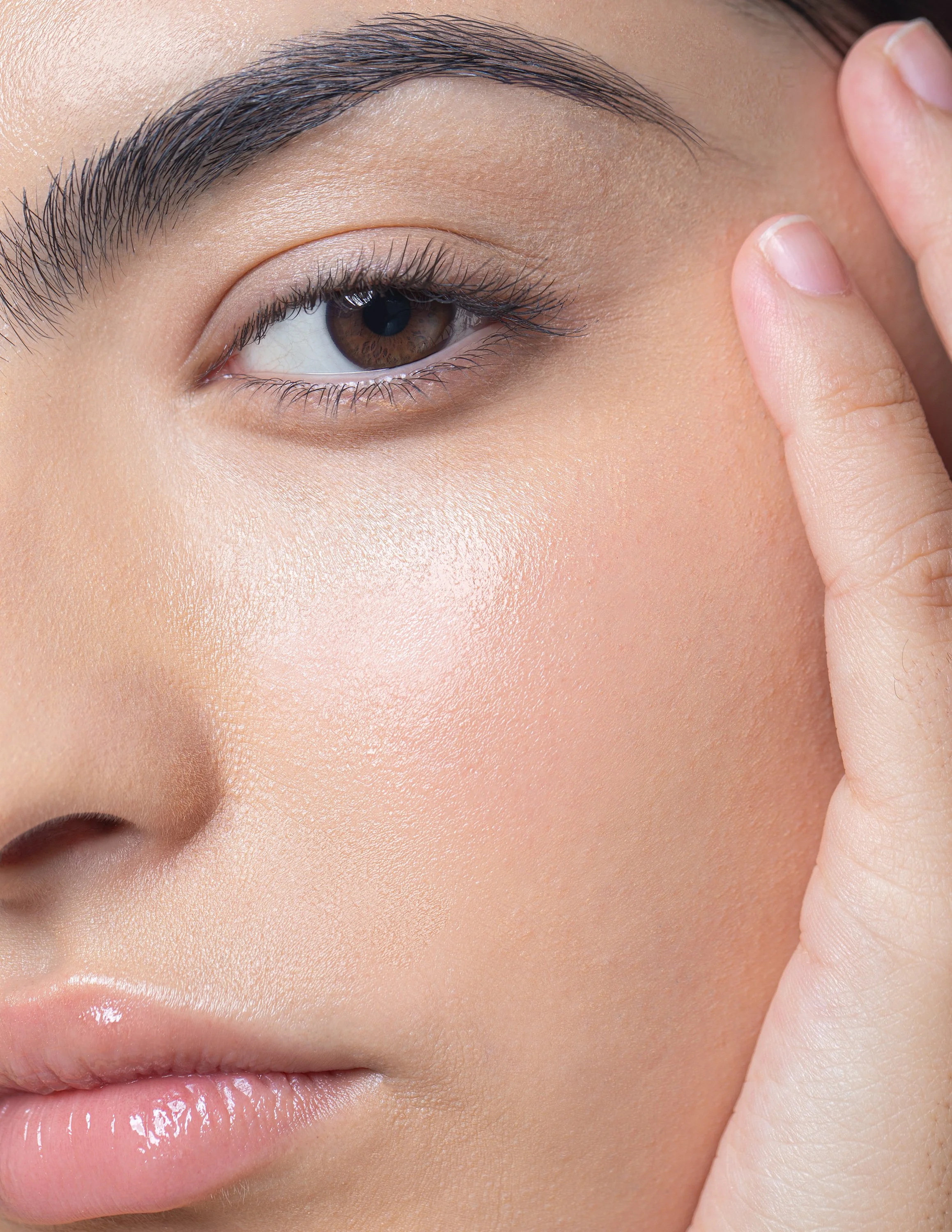 Close-up of a woman's face showing eye, eyebrow, cheek, and part of lips, with her hand touching her face.