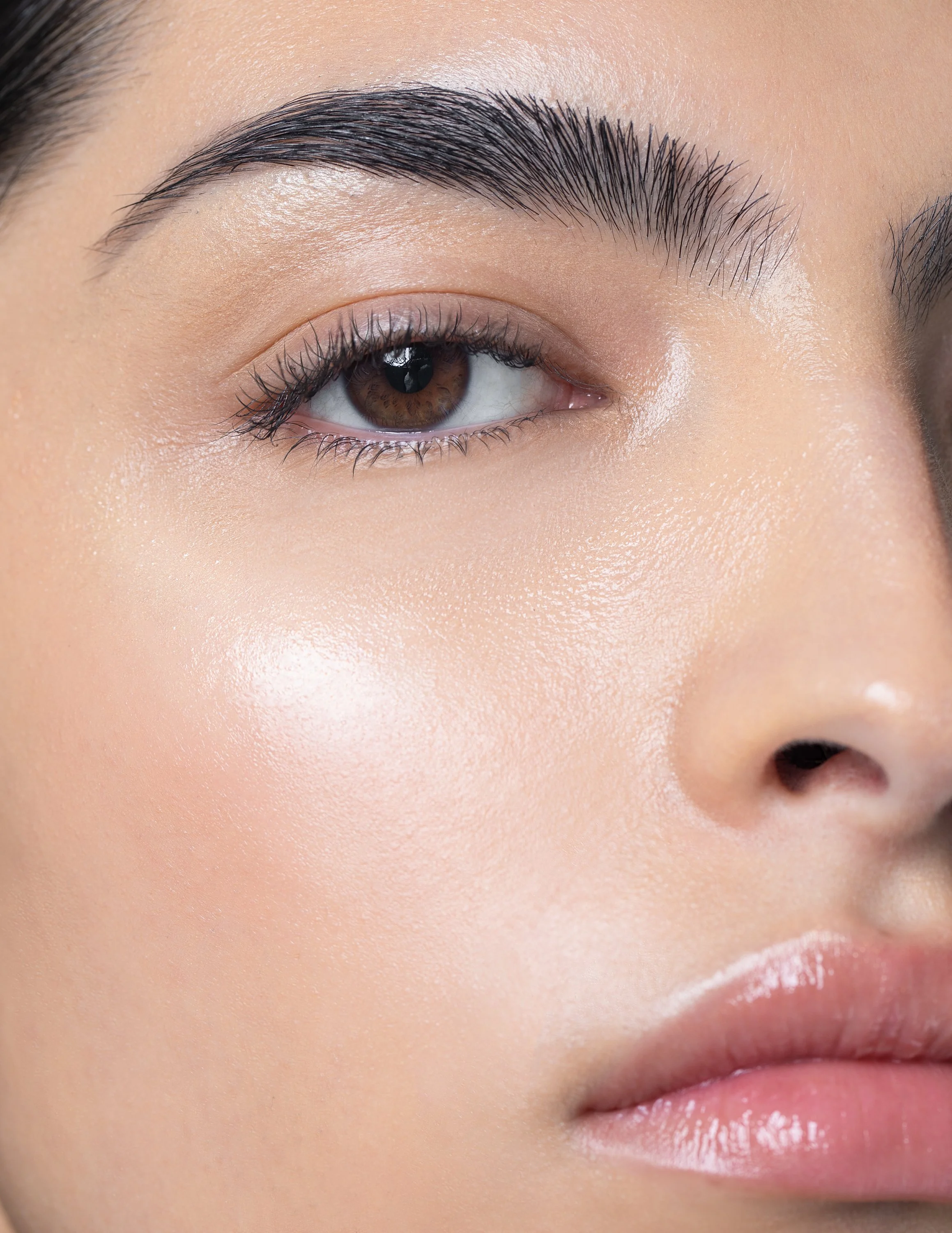 Close-up of a woman's face showing her eye, eyebrow, and part of her nose and lips, with clear skin and makeup.