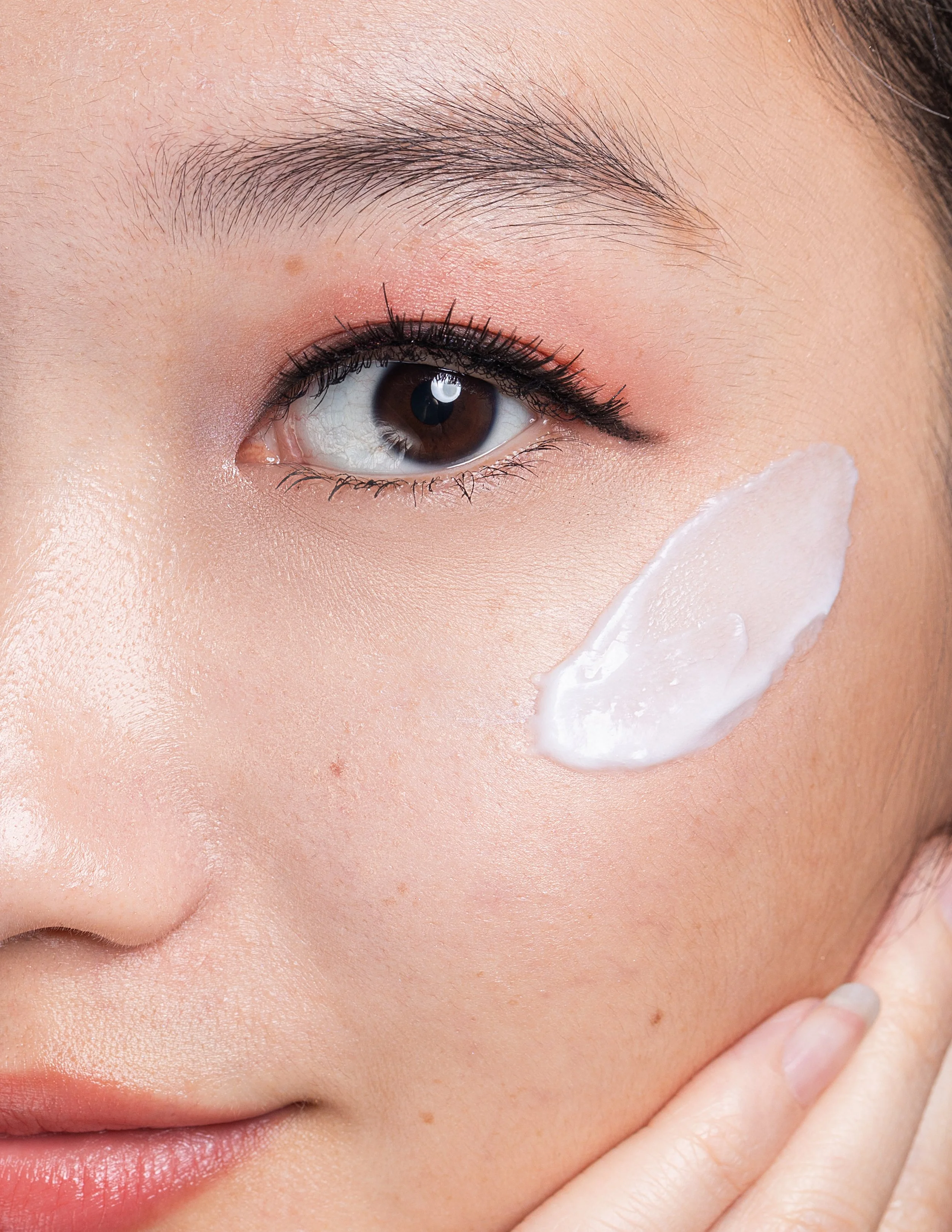 Close-up of a woman's face with a dollop of white cream on her cheek.