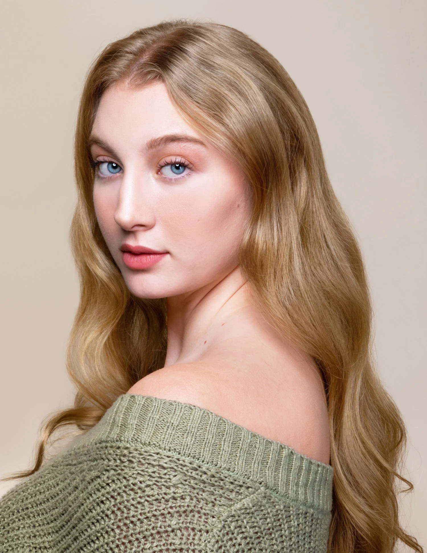 Close-up portrait of a young woman with long, wavy red hair and blue eyes, wearing a green knitted off-the-shoulder sweater.