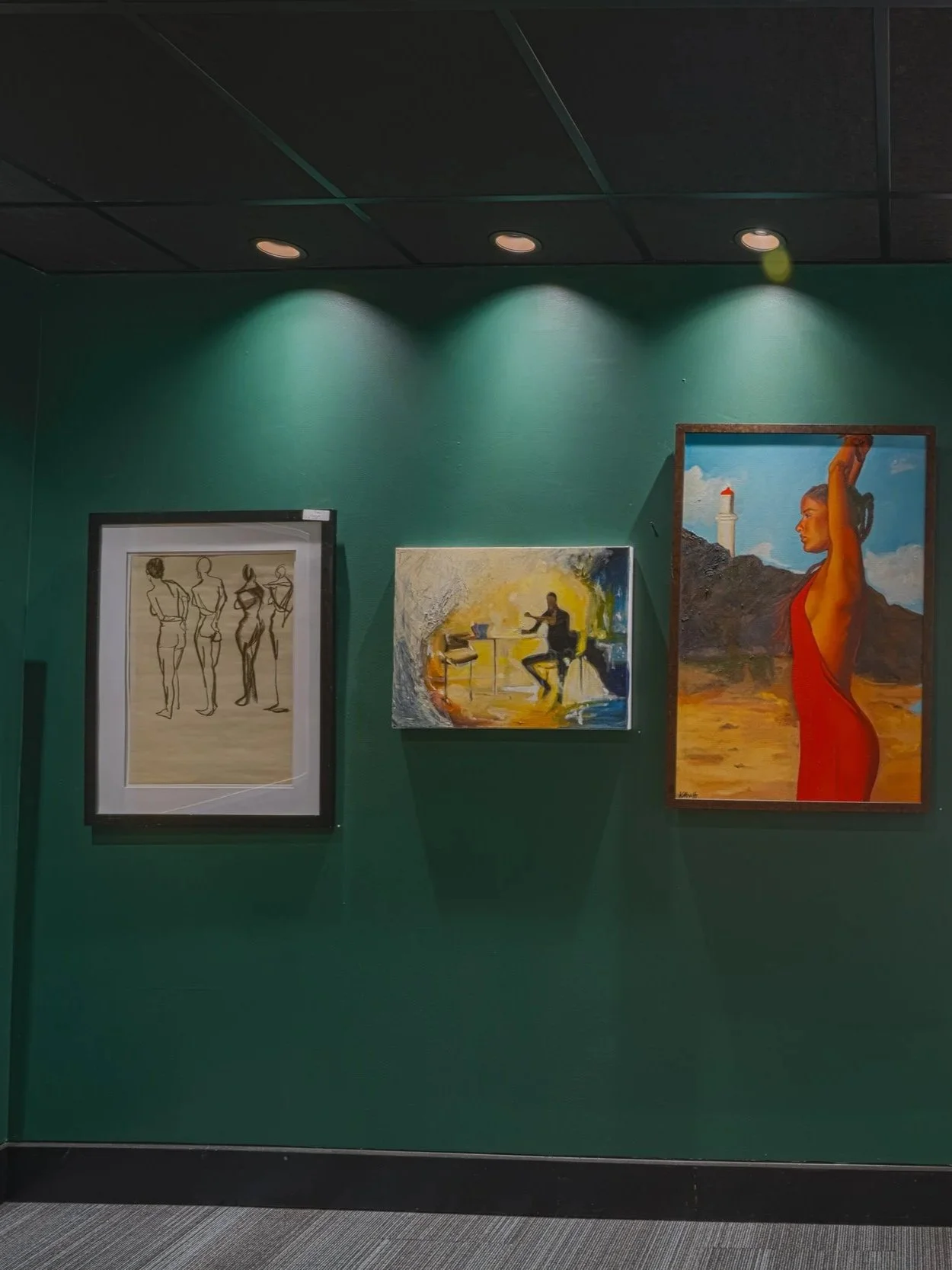 Three paintings hanging on a green gallery wall, illuminated by ceiling lights. The left painting depicts sketches of three women from behind, the middle painting shows two figures playing instruments, and the right painting features a woman in a red dress with a lighthouse in the background.