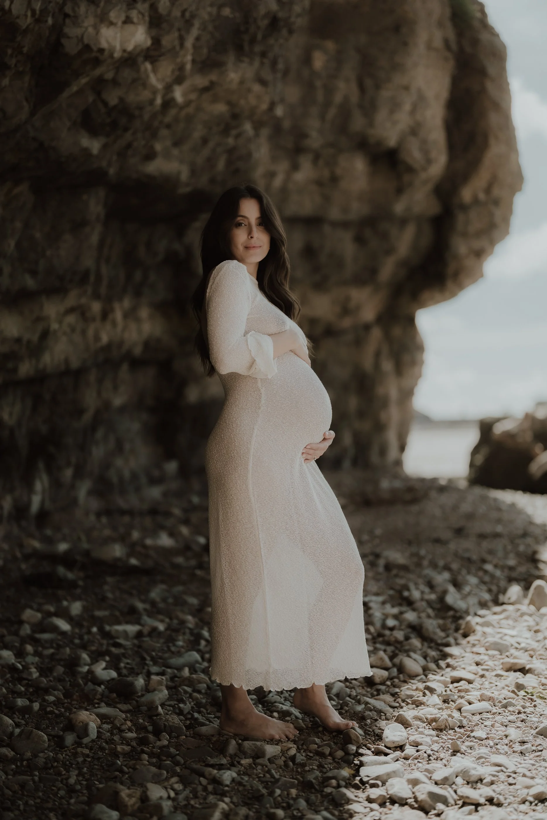 photograph of a pregnant woman at the beach wearing a white dress