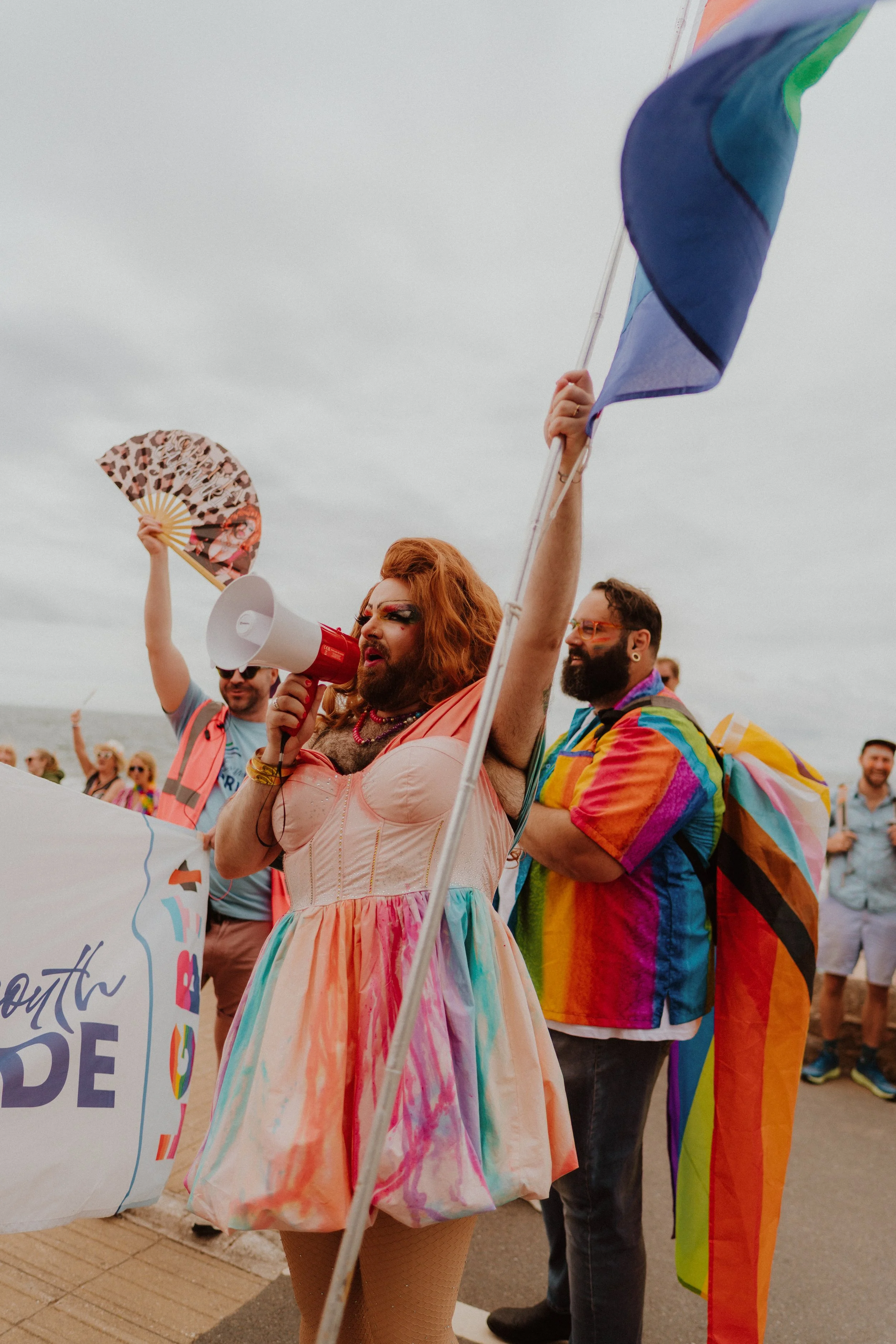 drag queen holding up the lgbtq flag during the pride march in exmouth