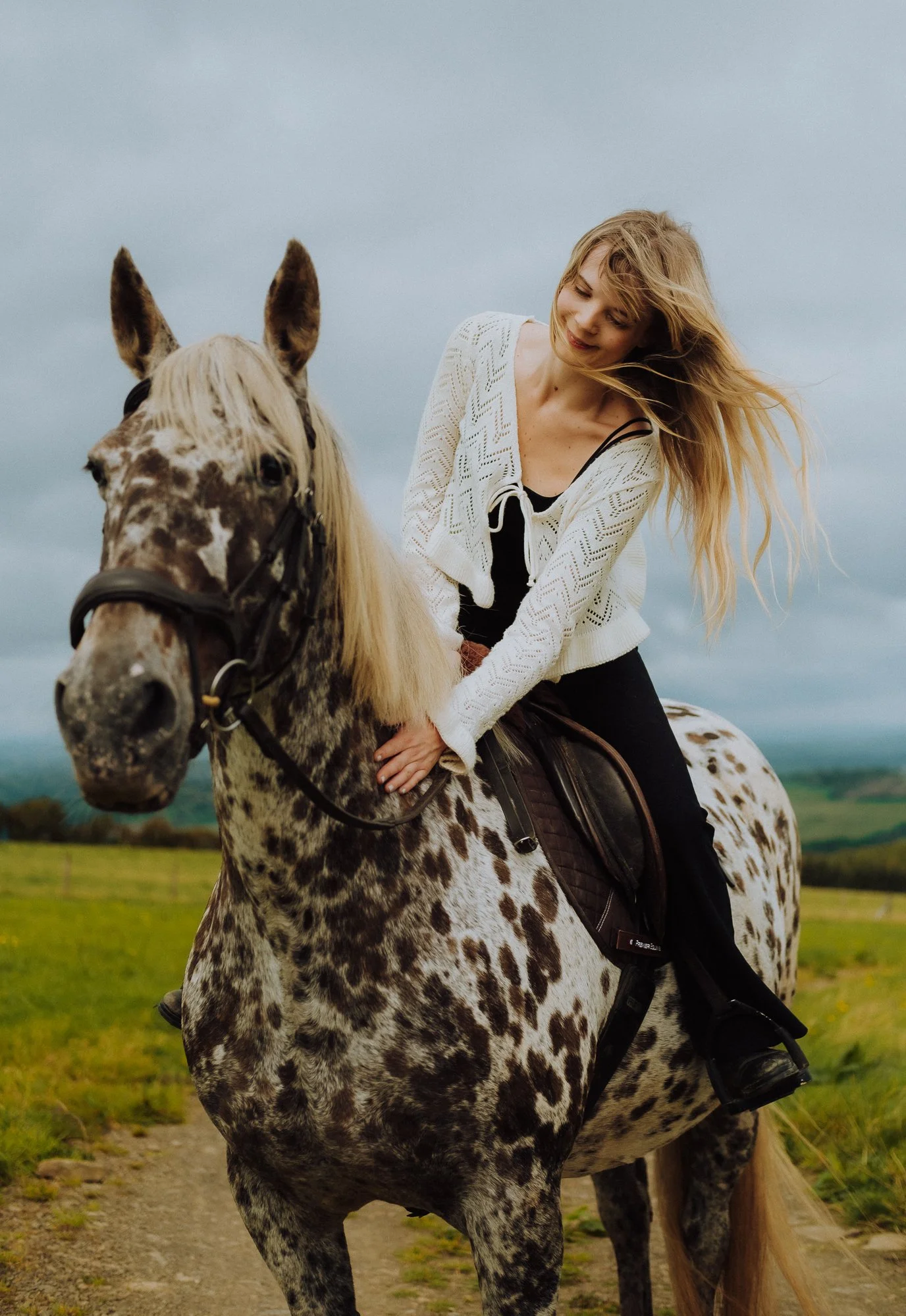 portrait of a woman riding her horse and smiling whilst stroking the horse
