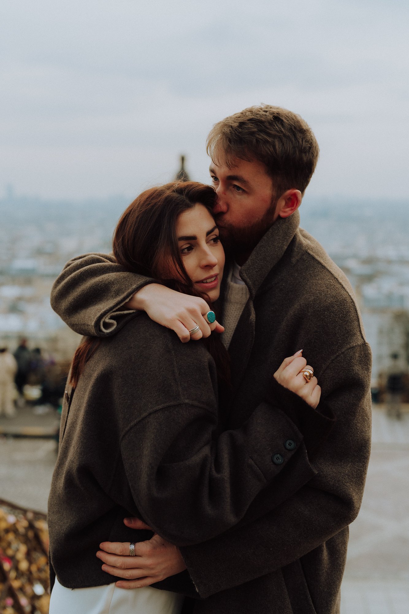 boyfriend kissing his girlfriend on the forehead with the view of paris behind