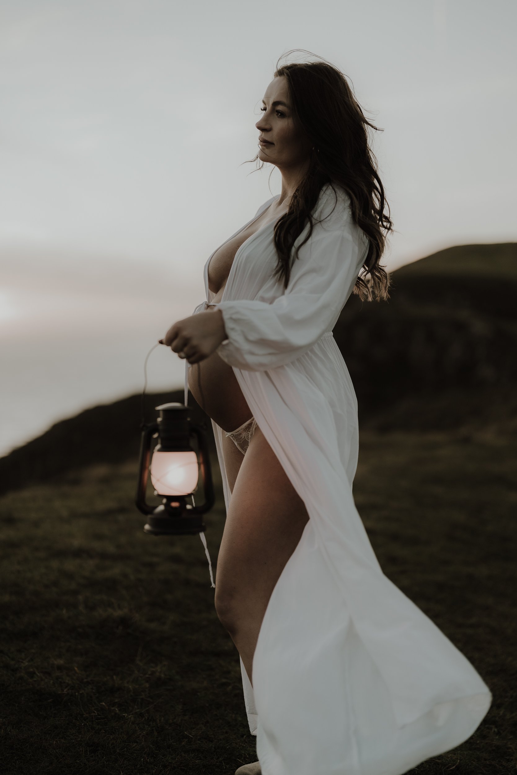 photograph of a pregnant woman on top of a cliff holding a lantern