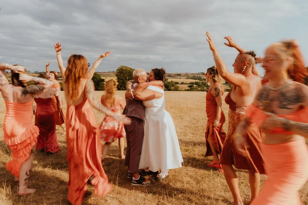 queer LGBTQIA+ wedding with best people dancing around the newlywed kissing