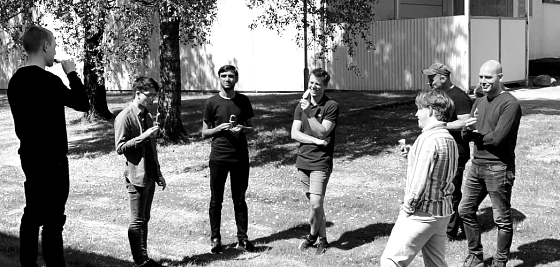 En gruppe mennesker står sammen utendørs, noen ser på mobiltelefoner og andre snakker.