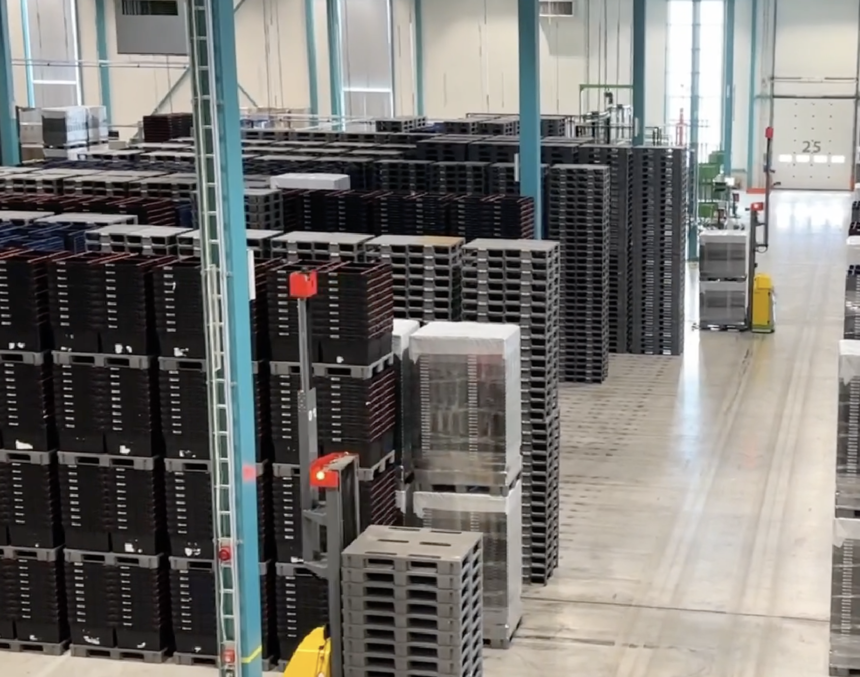 Lager med stabler av plastpaller, industrielle hylleplasser, og åpen gangvei. Lyse farger, industrielle byggematerialer.