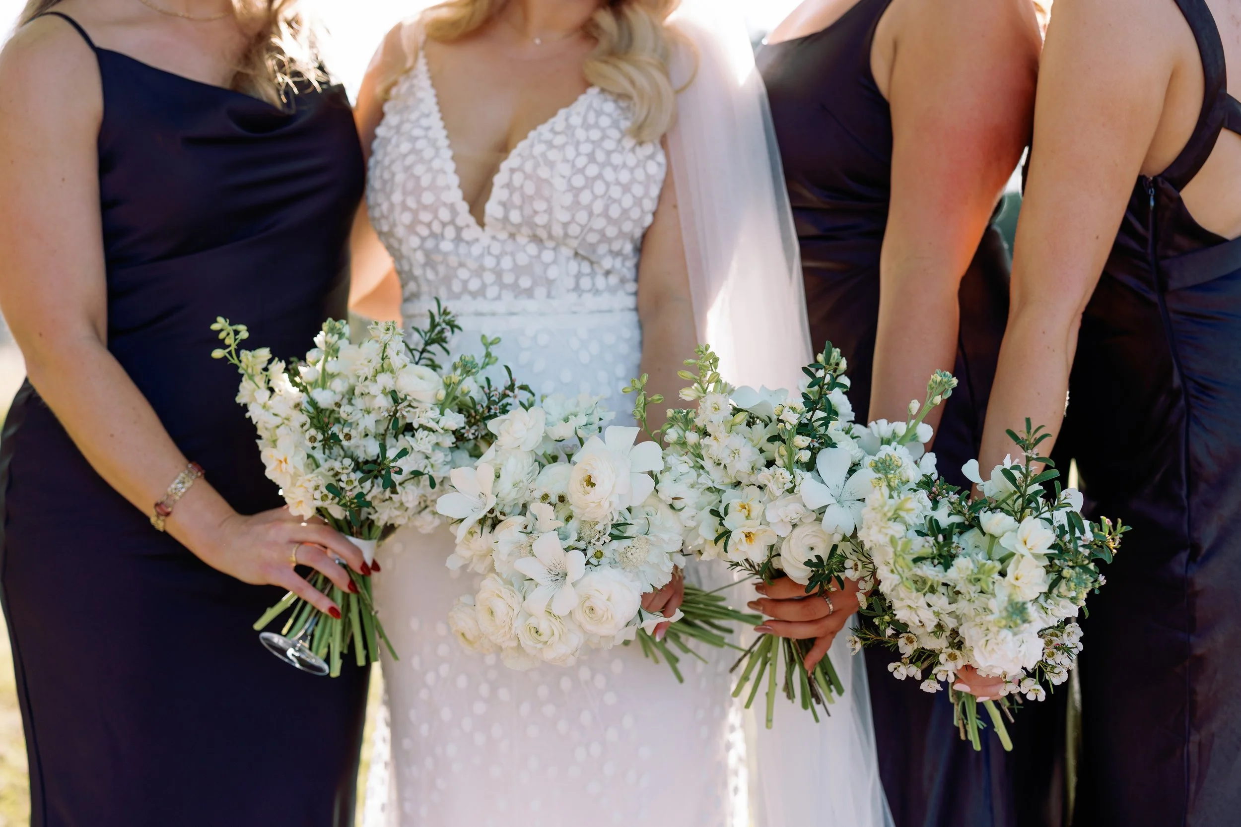 Close-up of a bride and bridesmaids holding bouquets of white flowers at a wedding.