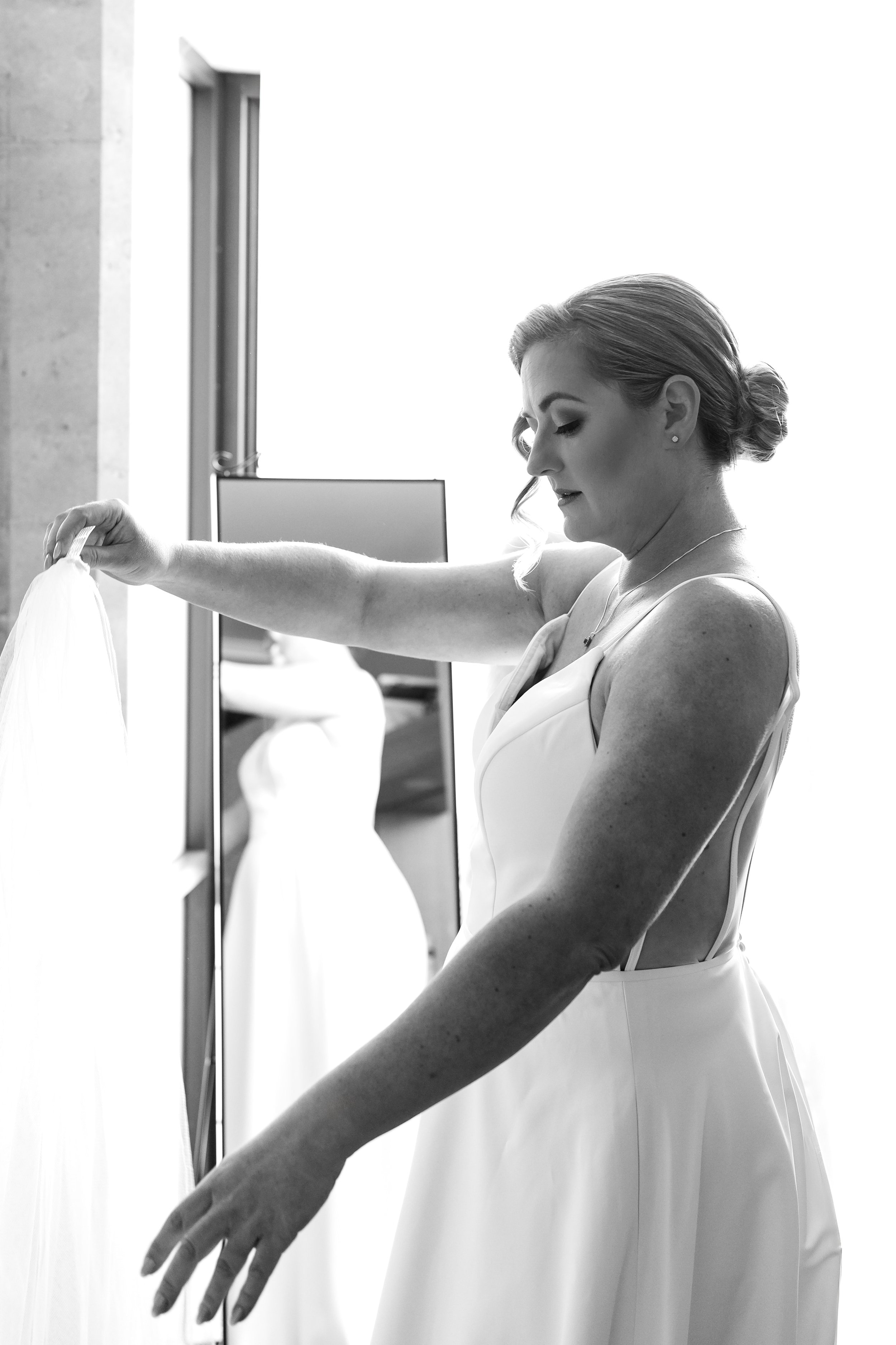 A woman in a white dress looking at a gown she is holding.