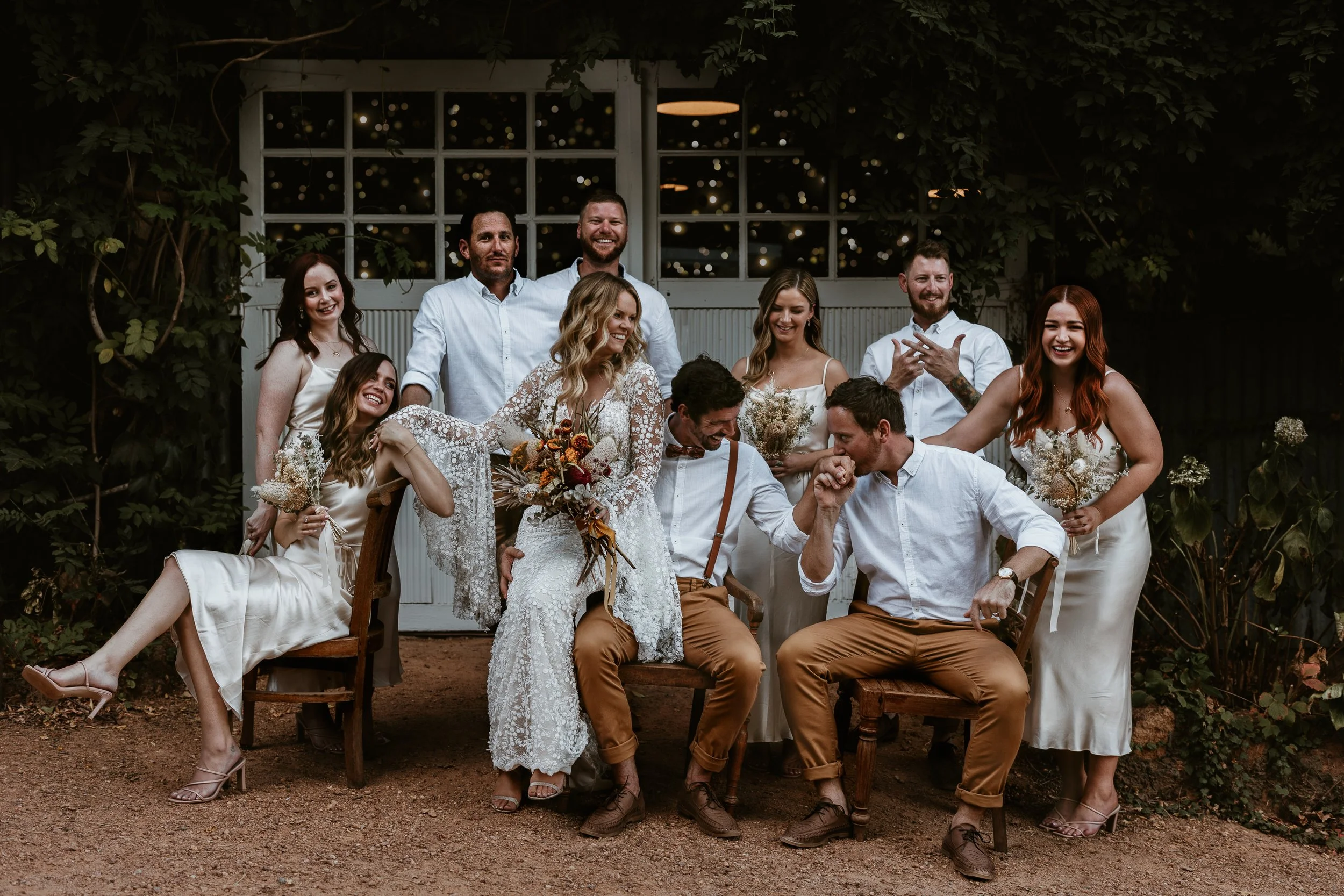 A group of people gathered outdoors for a wedding celebration, with some seated and others standing, all smiling and enjoying the moment.
