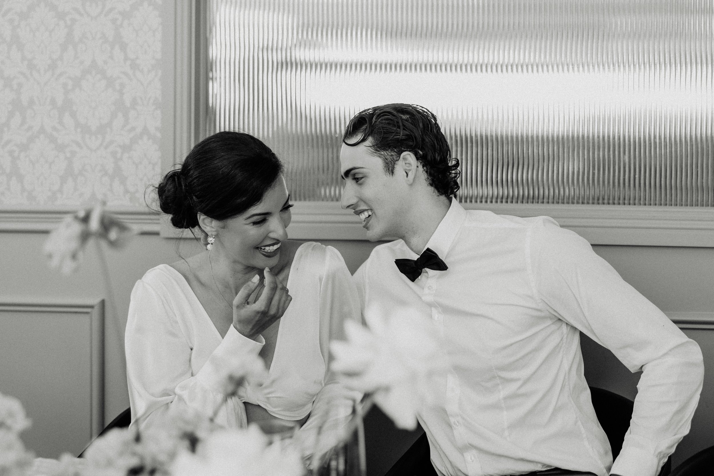 A black and white photo of a woman and a man smiling and leaning towards each other, dressed elegantly, at a formal event.
