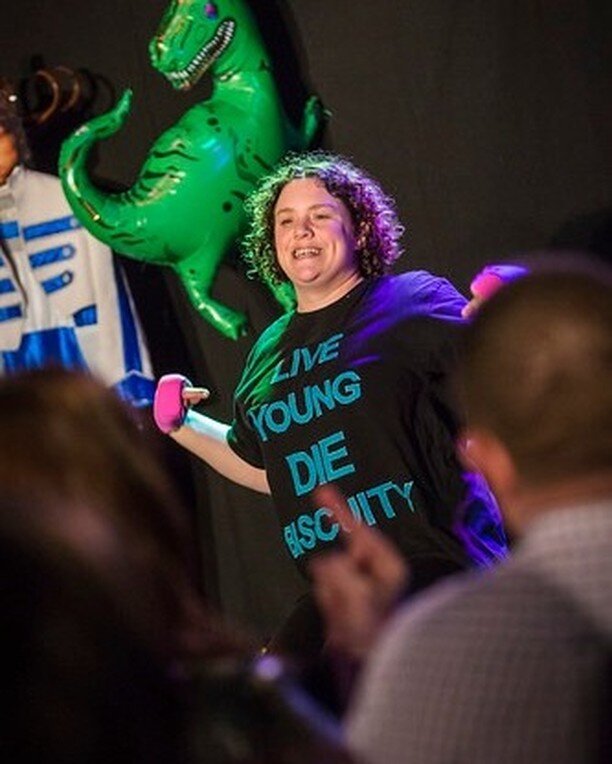 The answer is... Touretteshero  of course!!!

A majestic part of Jabberwocky Market🐉 with Backstage in Biscuit Land back in Spring 2016. 🍪 

Some of your suggestions were interesting! 😆

(image : a white, brown haired woman pointing at her black t